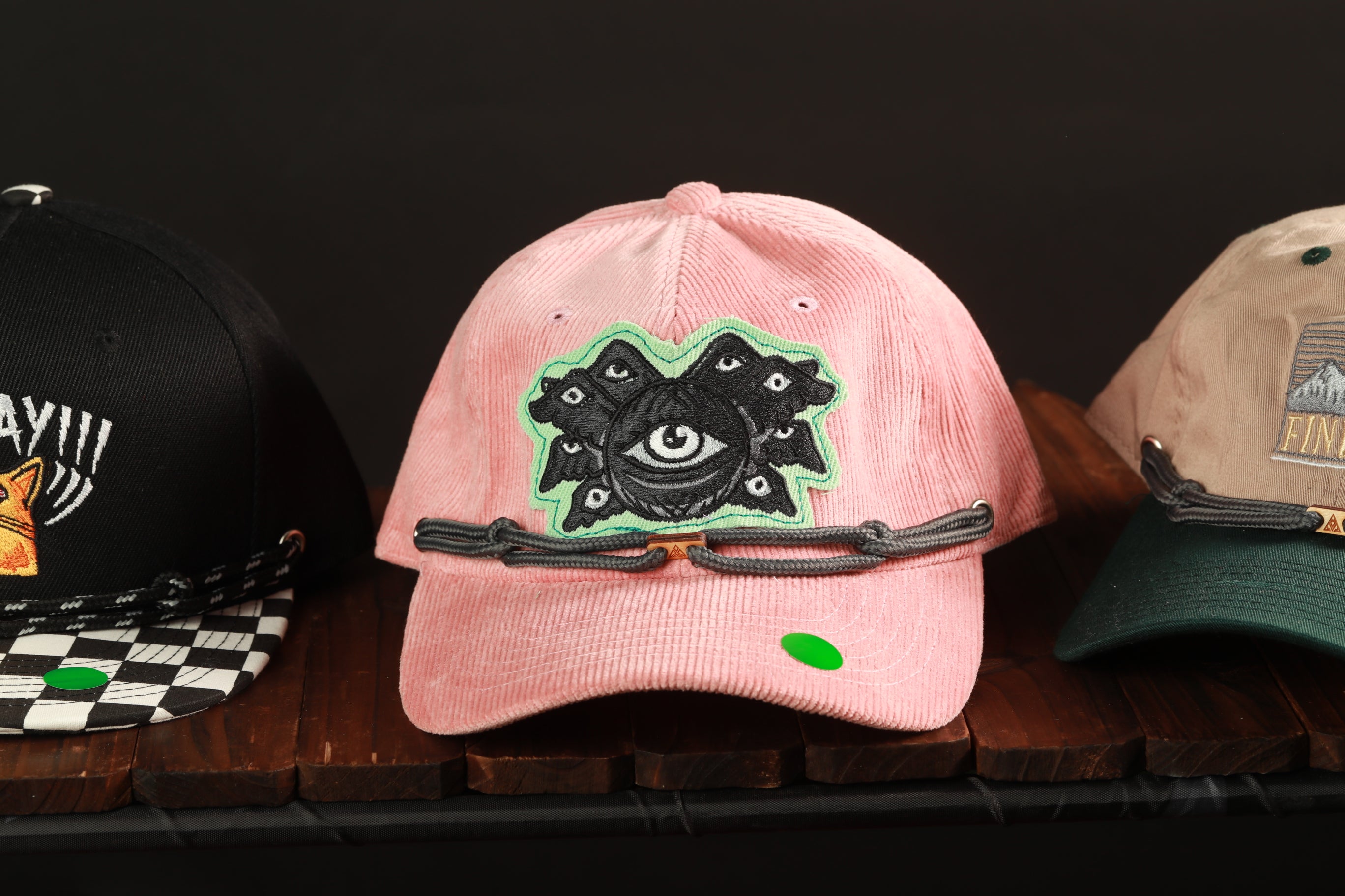Three baseball caps are displayed on a wooden surface, each with unique designs and colors.
