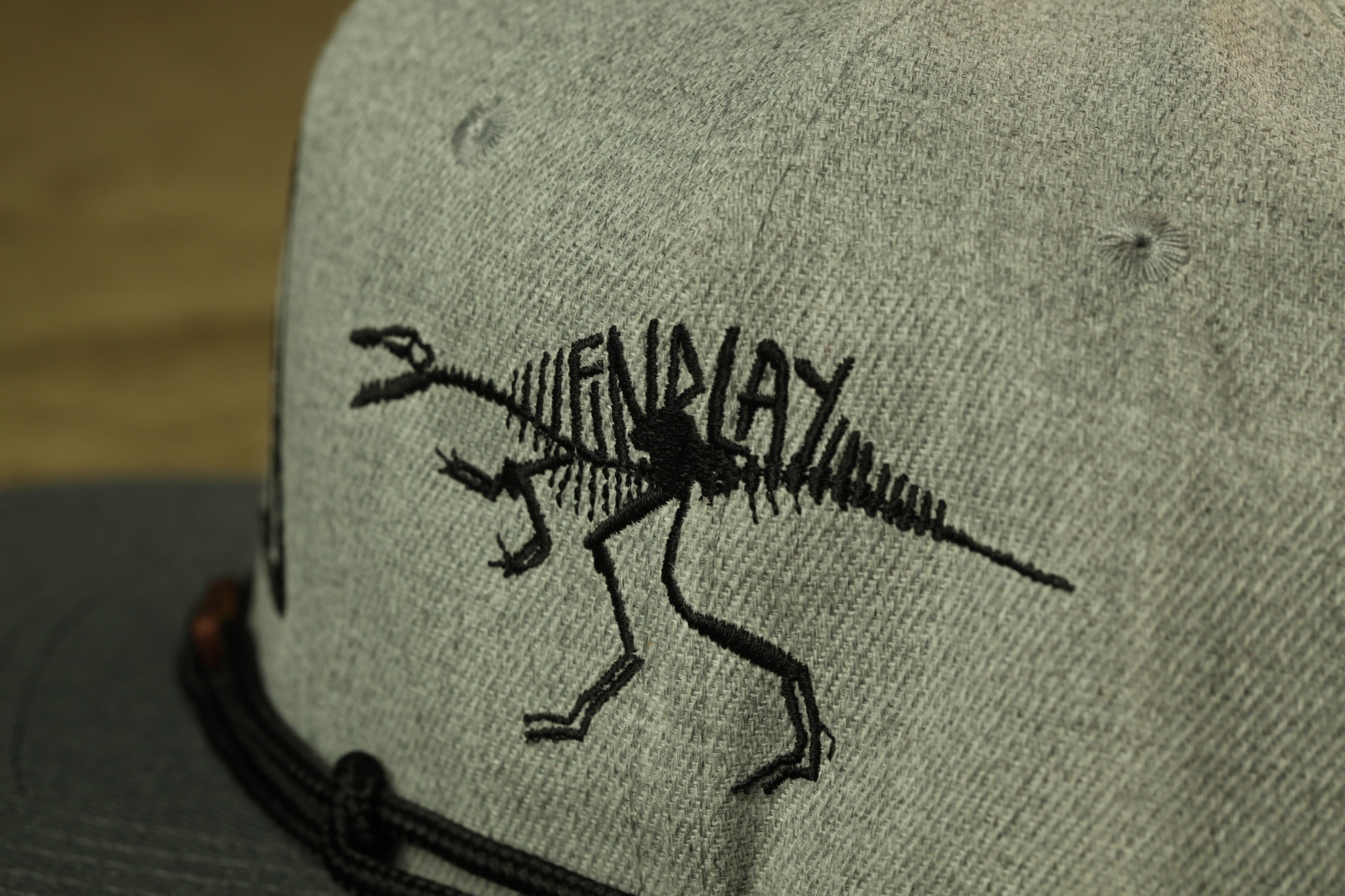 a grey baseball cap with a black dinosaur skeleton embroidered on it.