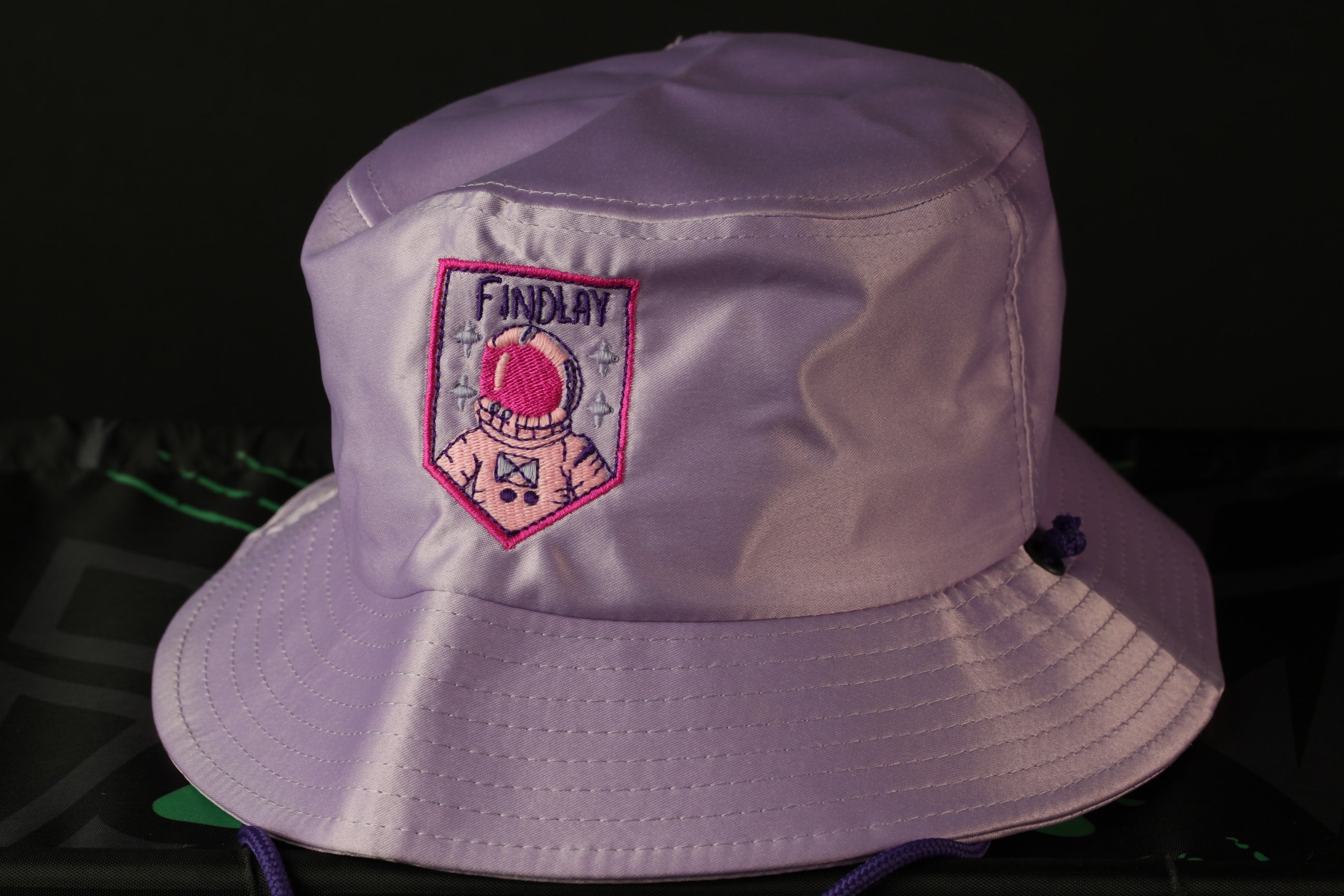 A purple bucket hat with a pink and purple embroidered patch that says "FINDLAY" on the front.