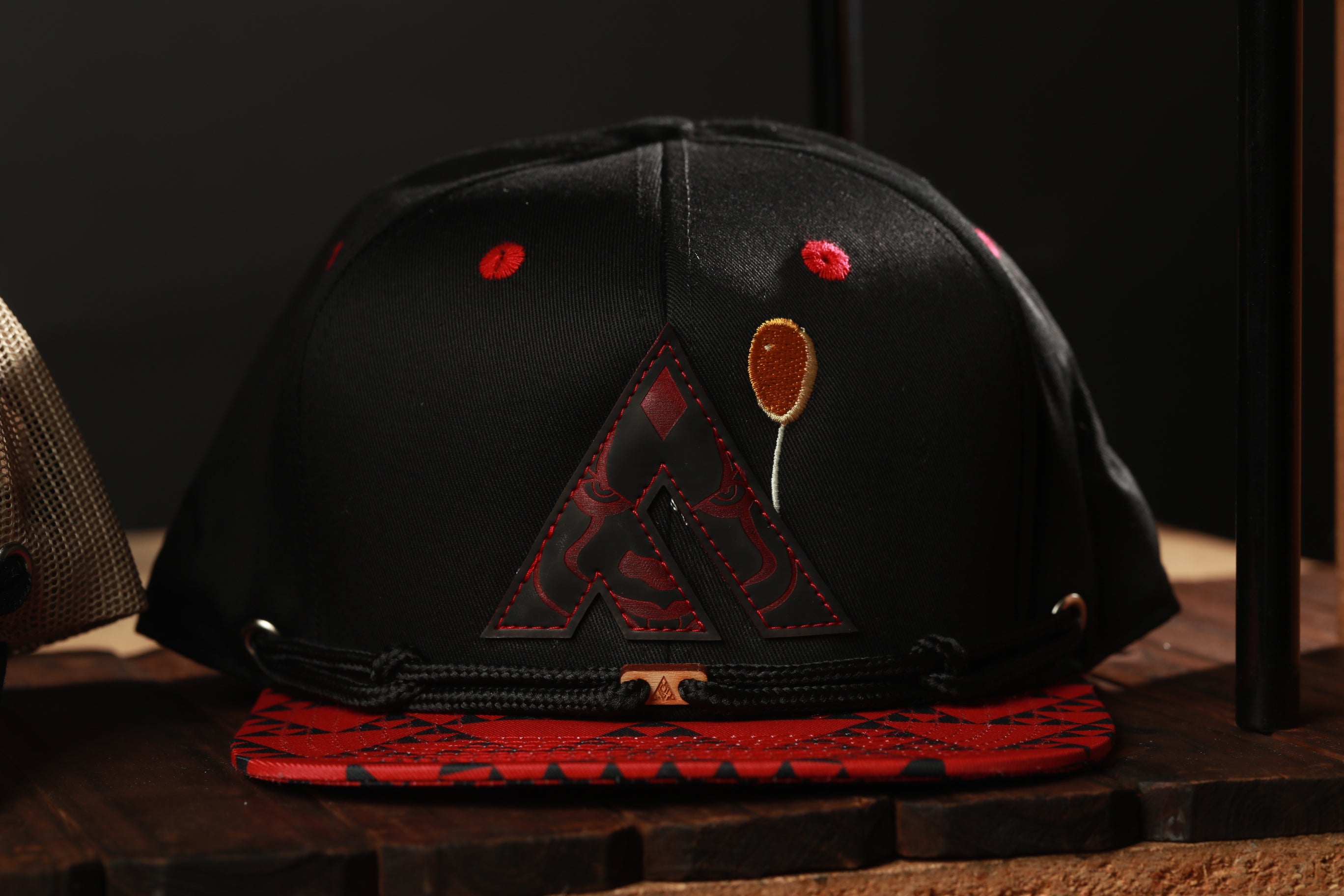 A black baseball cap with red accents and a red and black patterned fabric on the front.