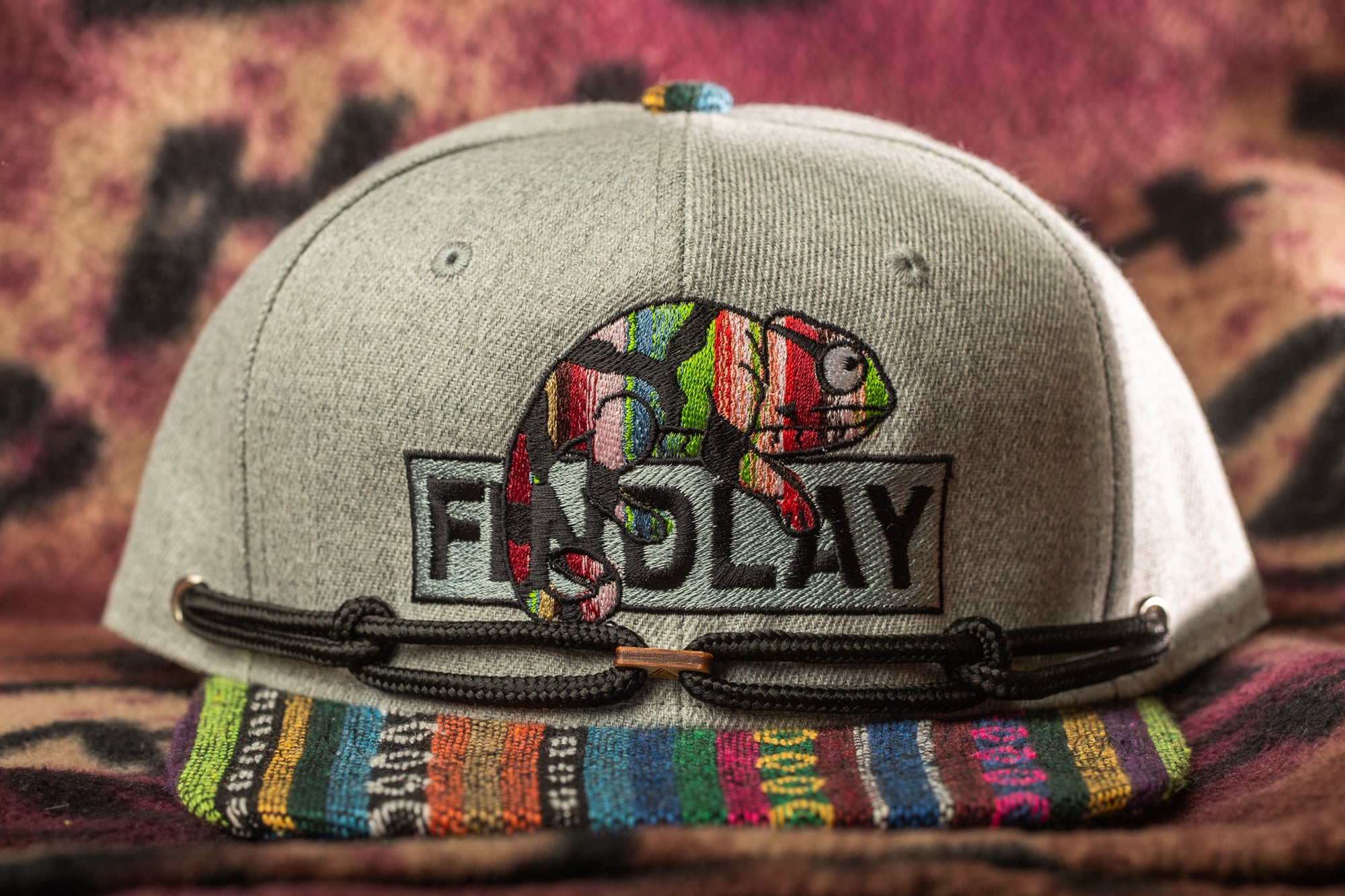 A gray baseball cap with a colorful, embroidered chameleon design and the word "FIND LAY" printed on it.