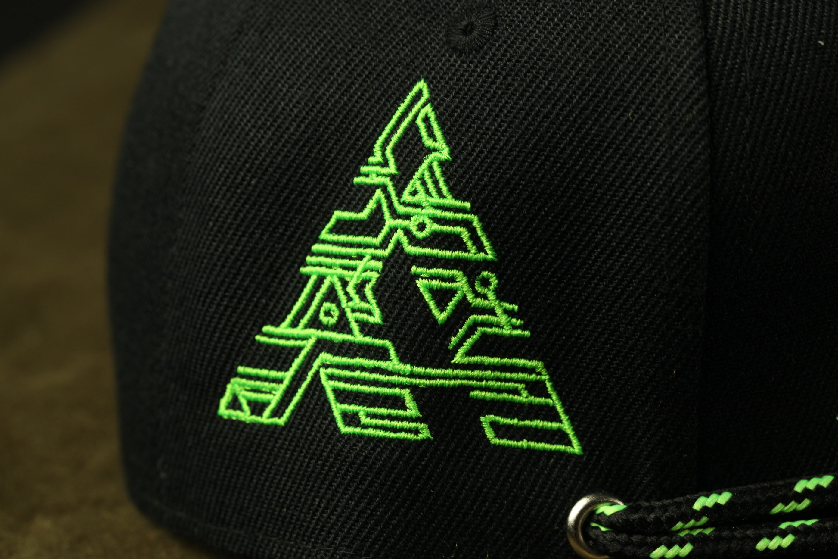 a close-up view of a black baseball cap with a green embroidered logo on the front.