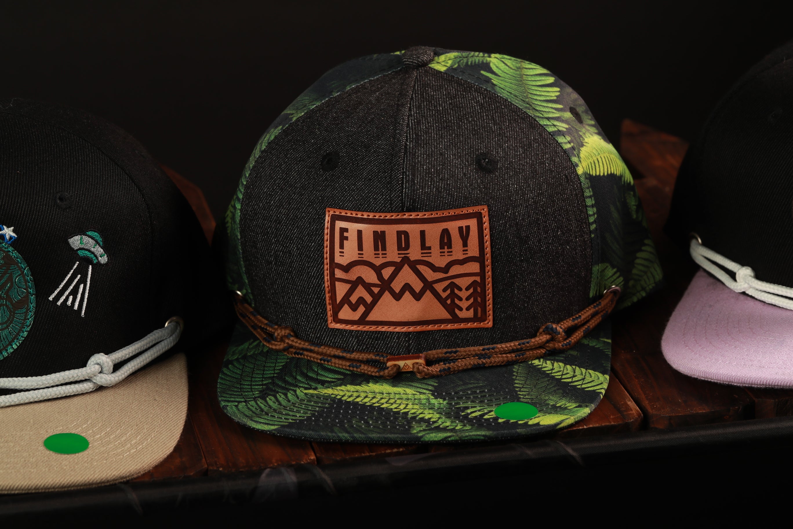 A collection of three baseball caps, each with unique designs and colors, displayed on a wooden surface.