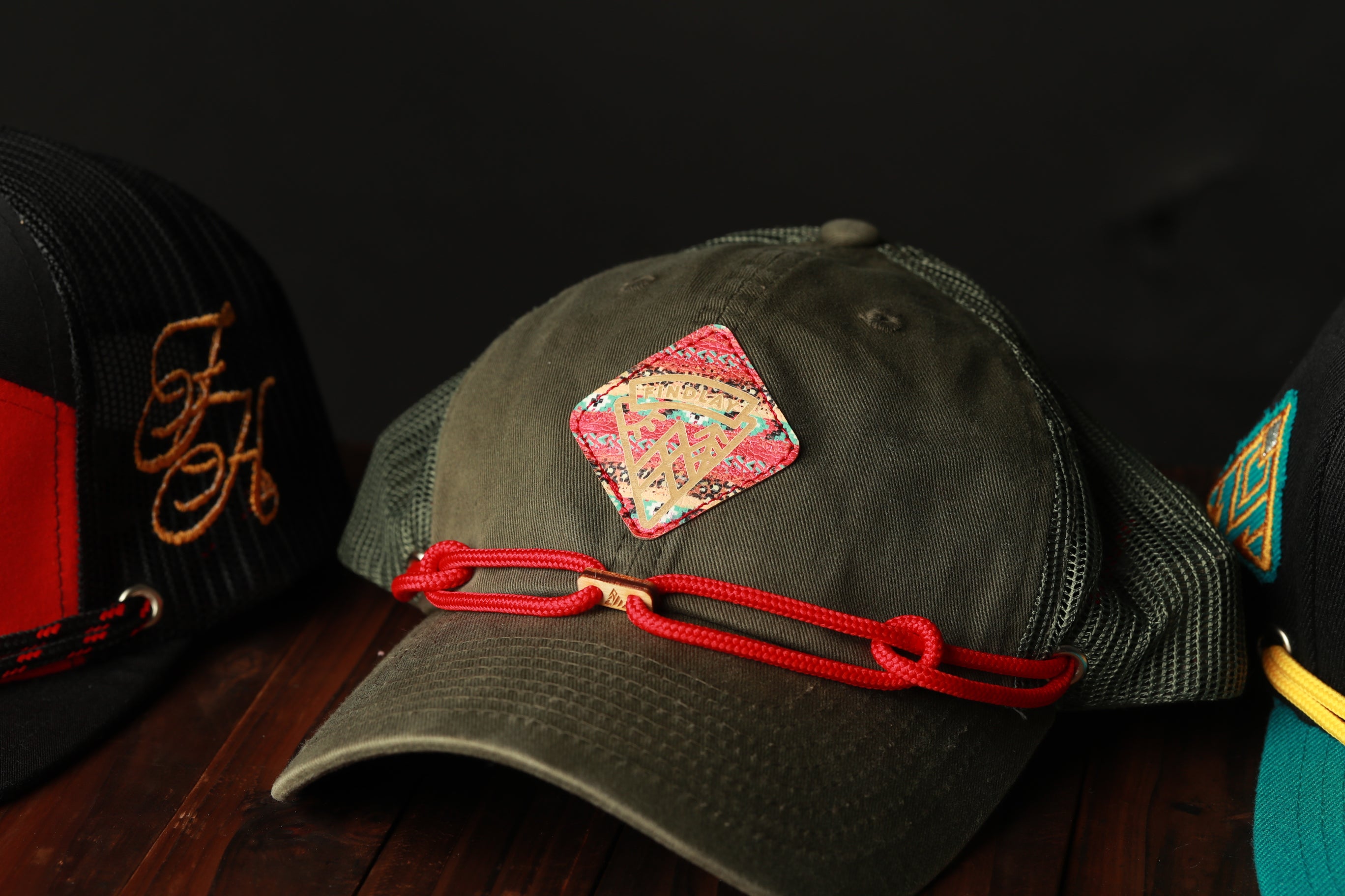 A close-up image of a green baseball cap with a red string and a decorative patch on the front, displayed on a wooden surface.