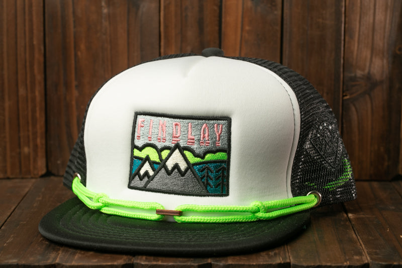 A white baseball cap with a graphic design and a green strap, placed on a wooden surface.