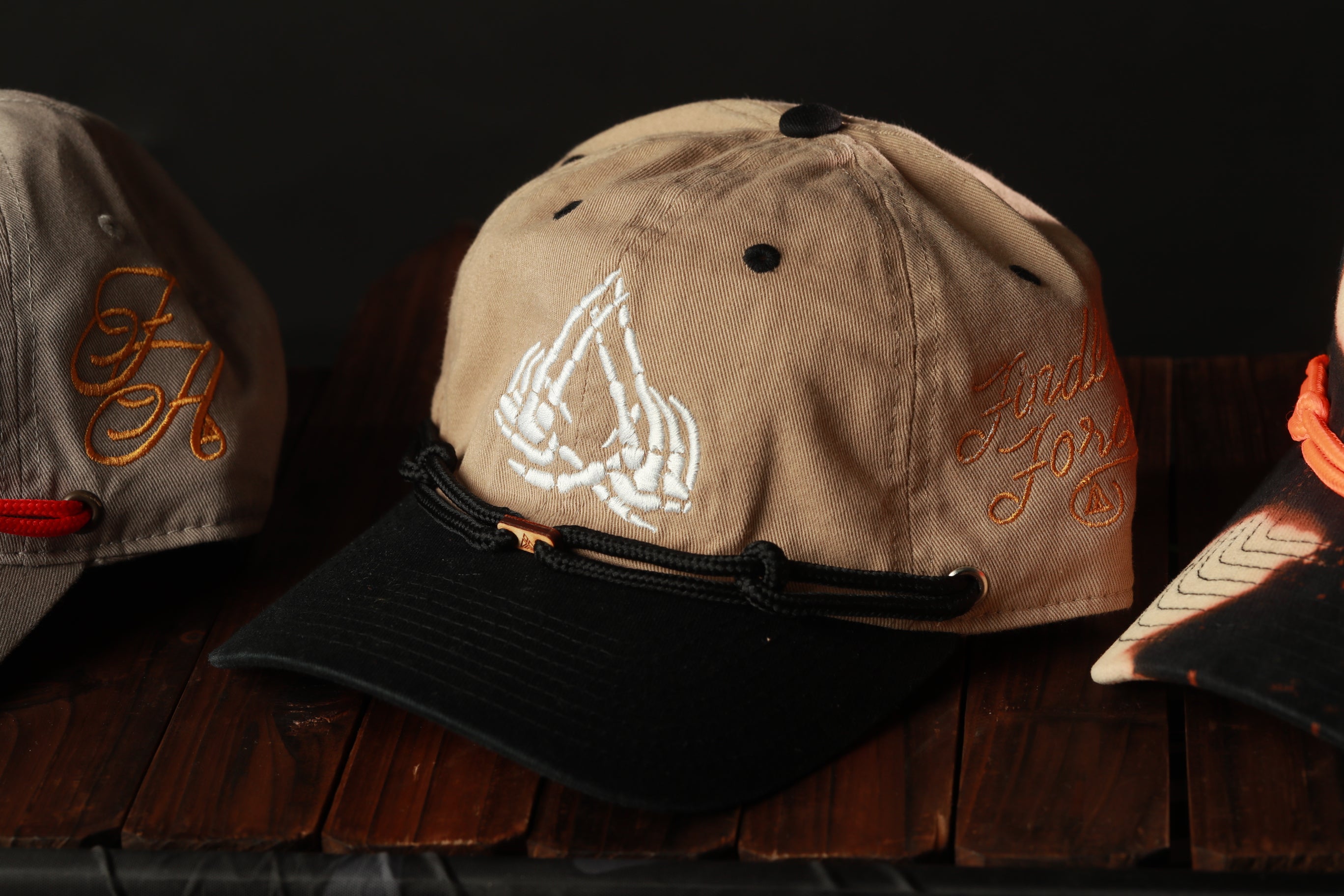 A beige baseball cap with a black brim and a white skull design on the front, sitting on a wooden surface.