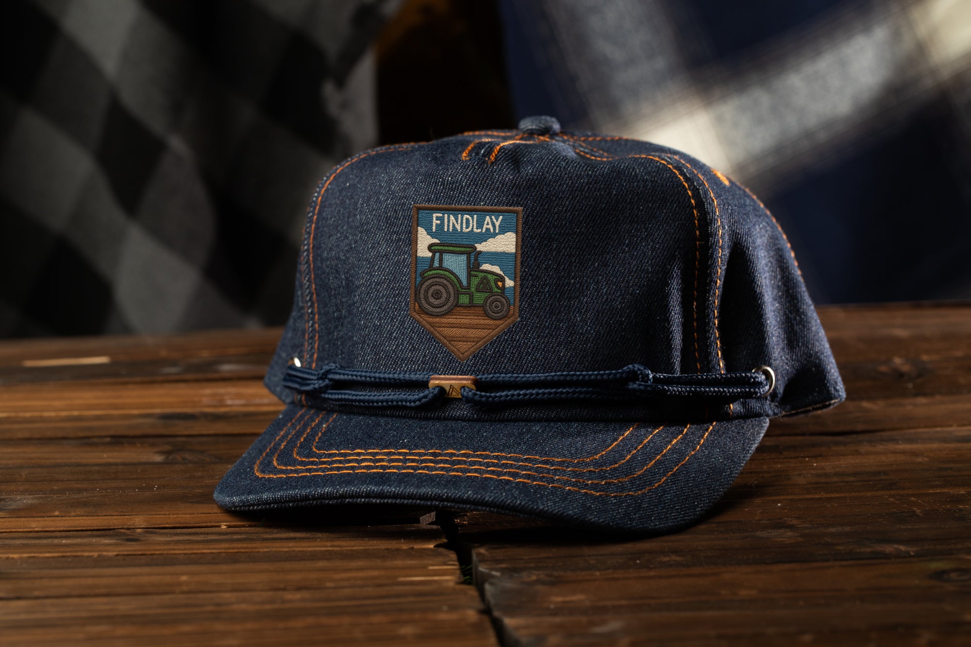A denim baseball cap with a tractor patch on it, placed on a wooden surface.