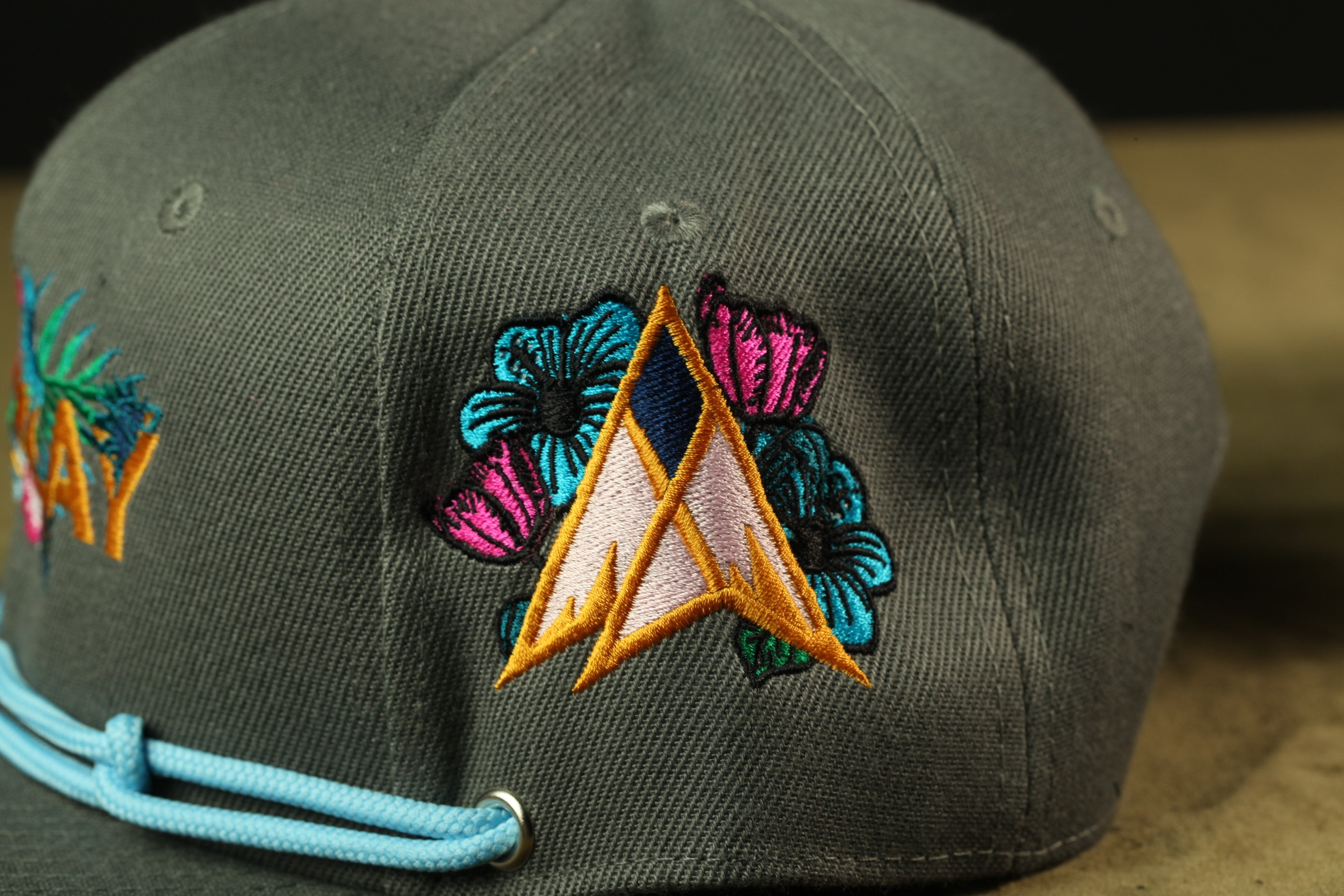 A close-up view of a gray baseball cap with colorful floral embroidery on the front.