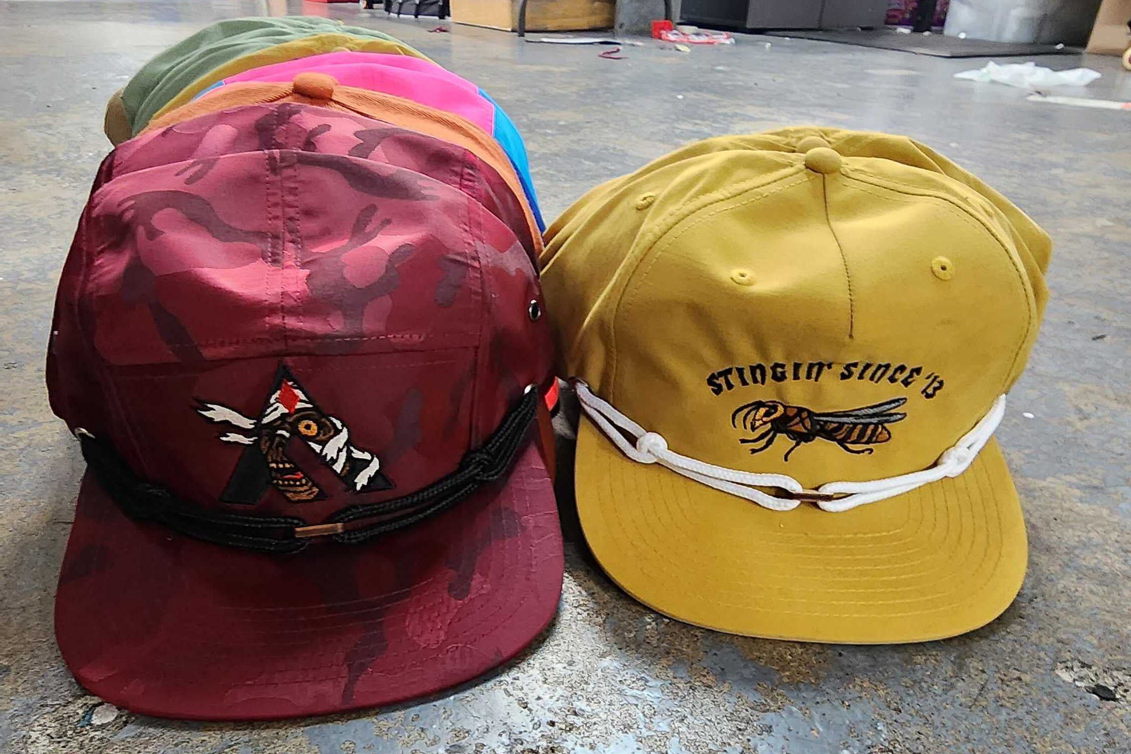 Two baseball caps, one red and one yellow, are sitting on a concrete surface.