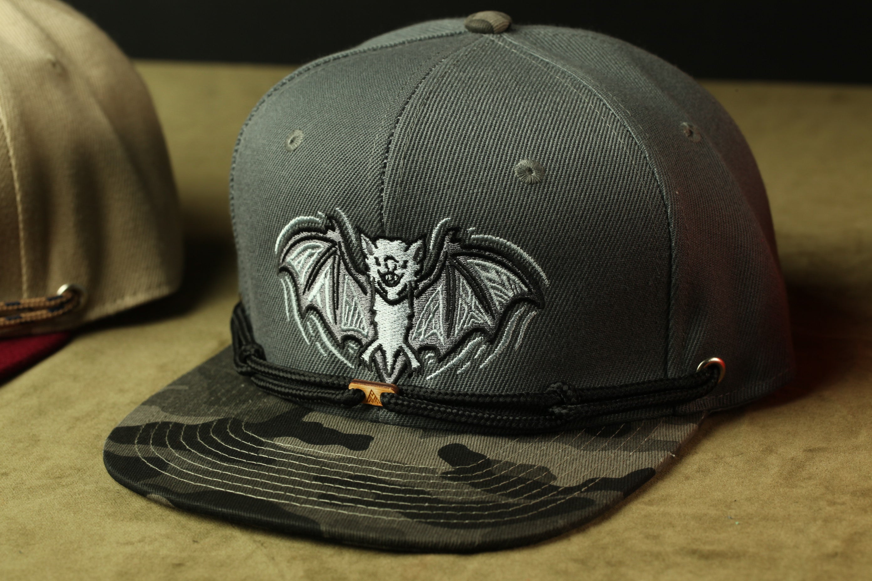 A gray baseball cap with a bat embroidered on it, sitting on a surface.