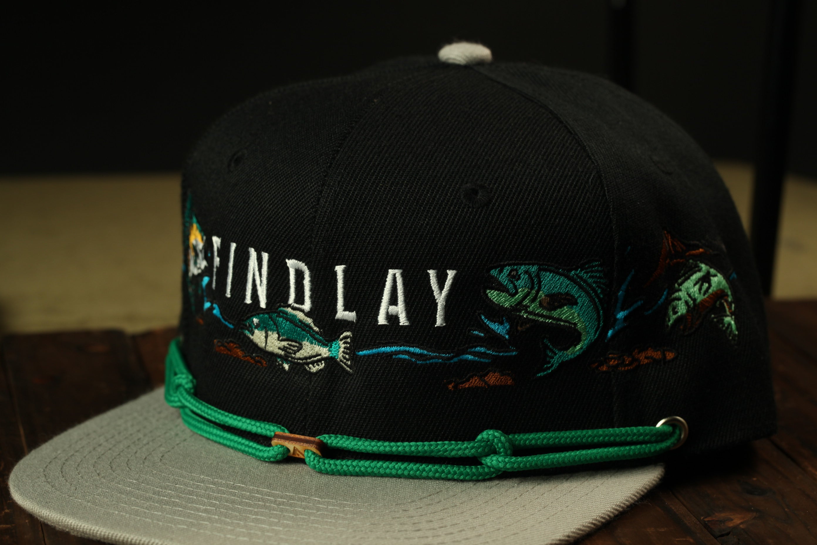 A black baseball cap with the word "FINDLAY" embroidered on it, along with fish designs.