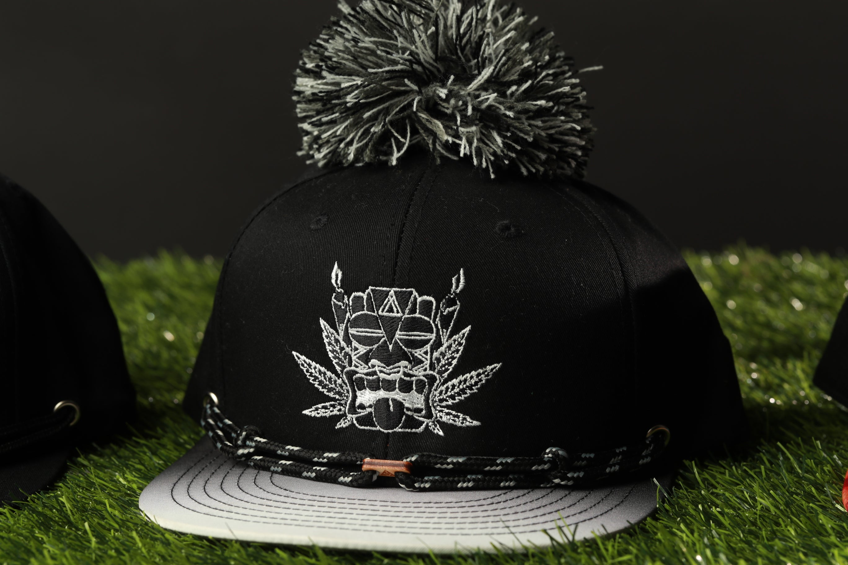 A black baseball cap with a white pom pom on top, featuring a graphic design on the front.