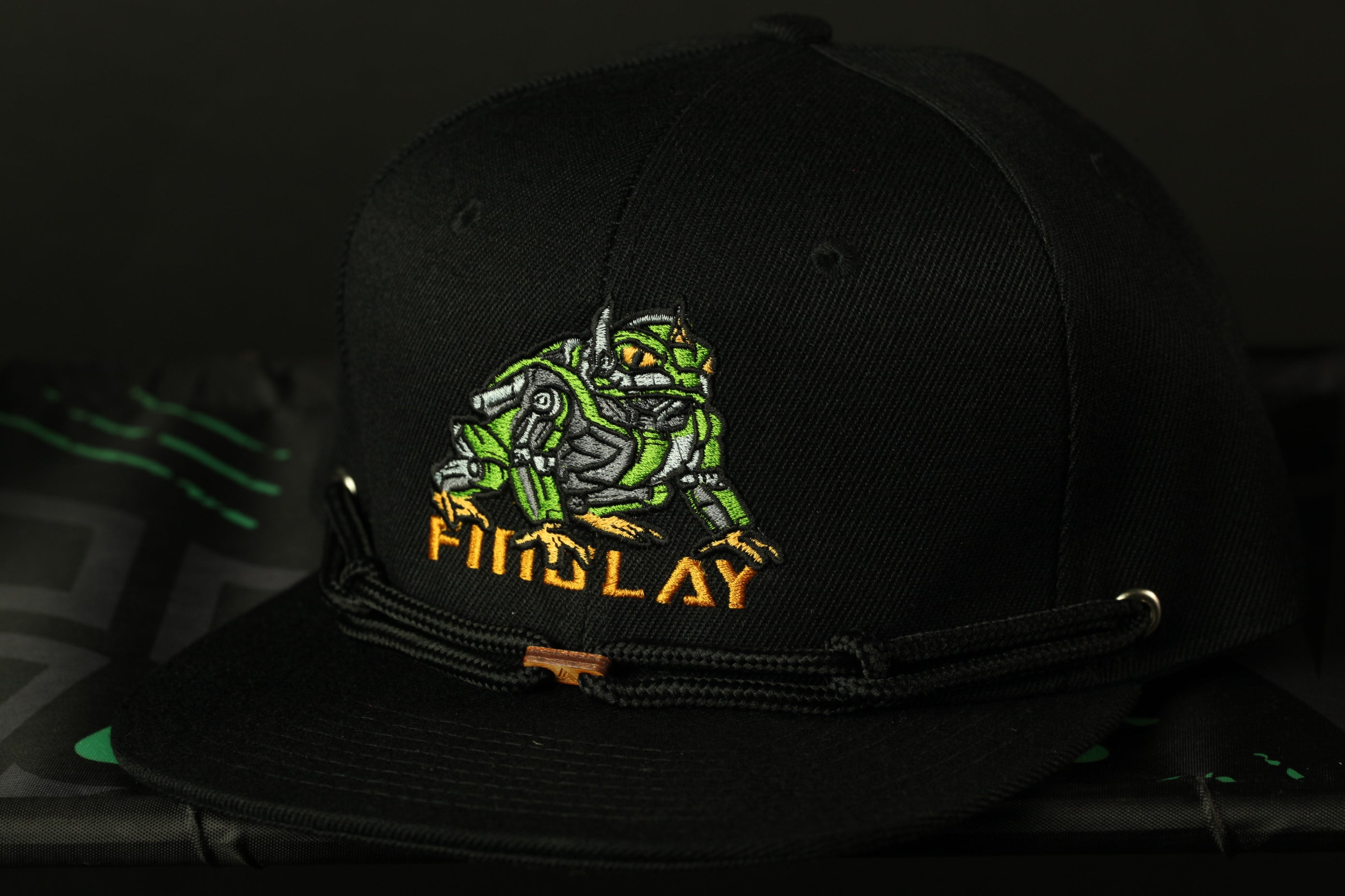 A black baseball cap with a green and yellow robot-like design on it.