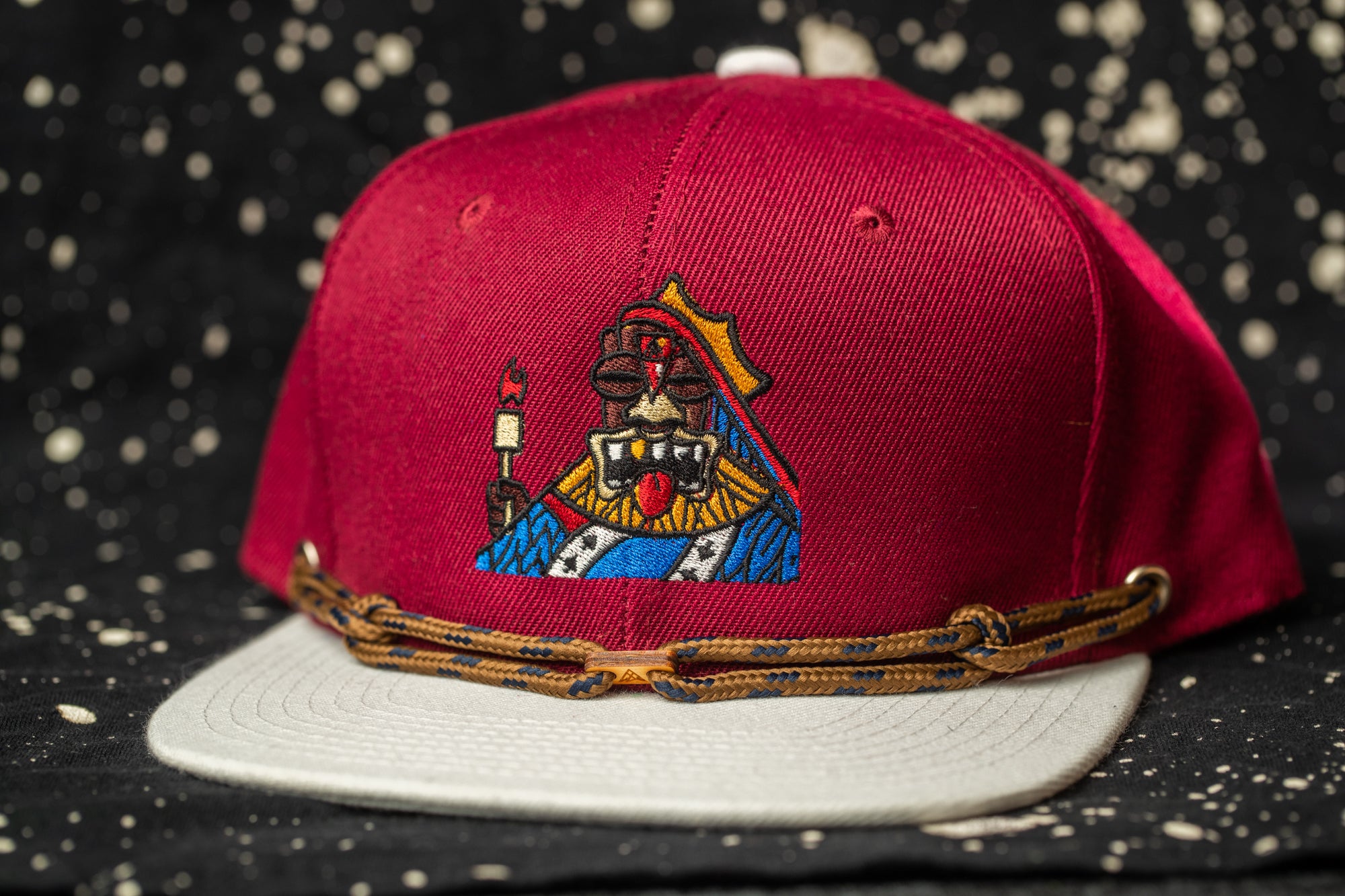 A red baseball cap with a colorful embroidered design on the front, featuring a stylized figure holding a red flag.