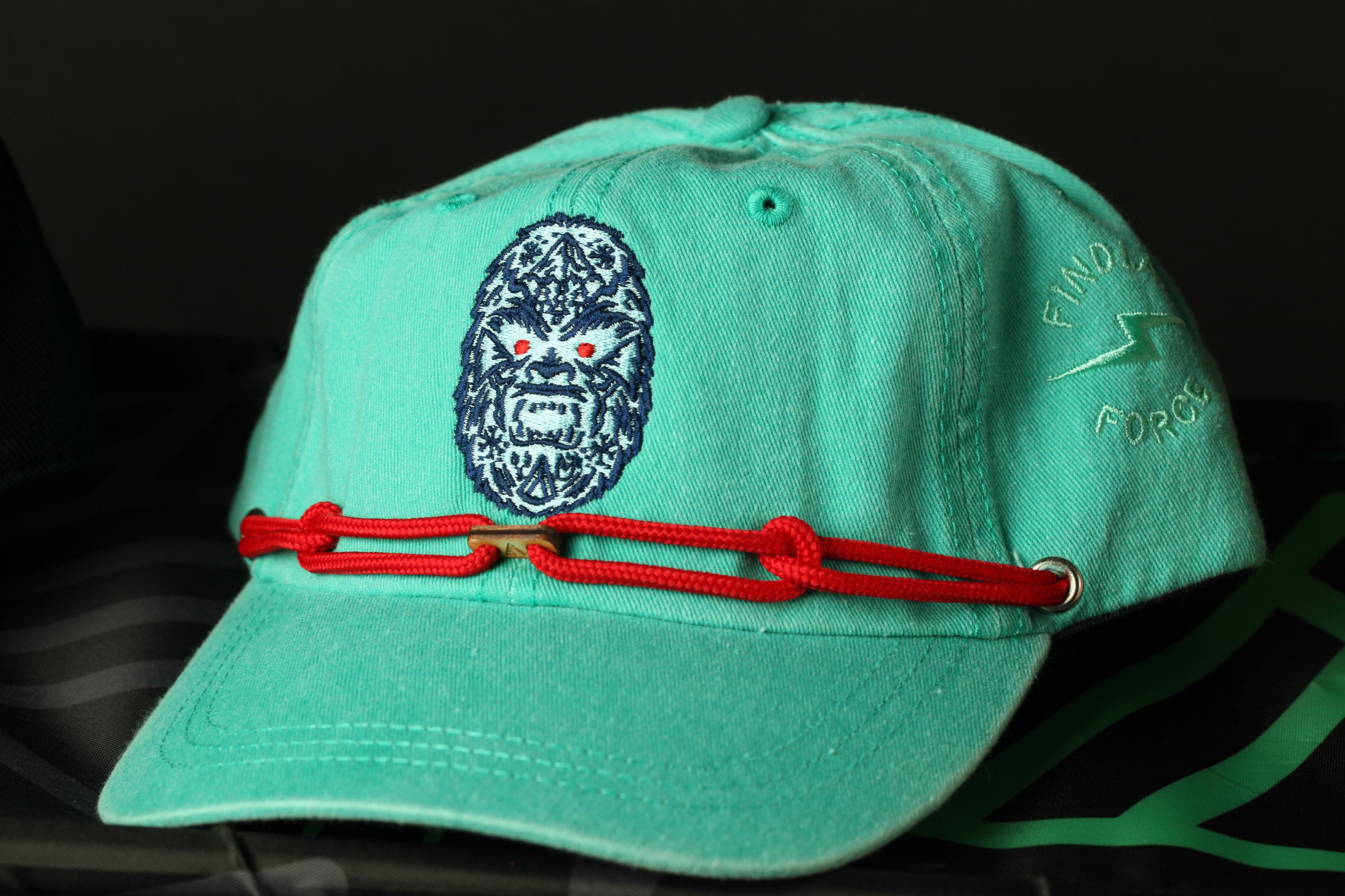 A turquoise baseball cap with a red string and a graphic of a gorilla on the front.