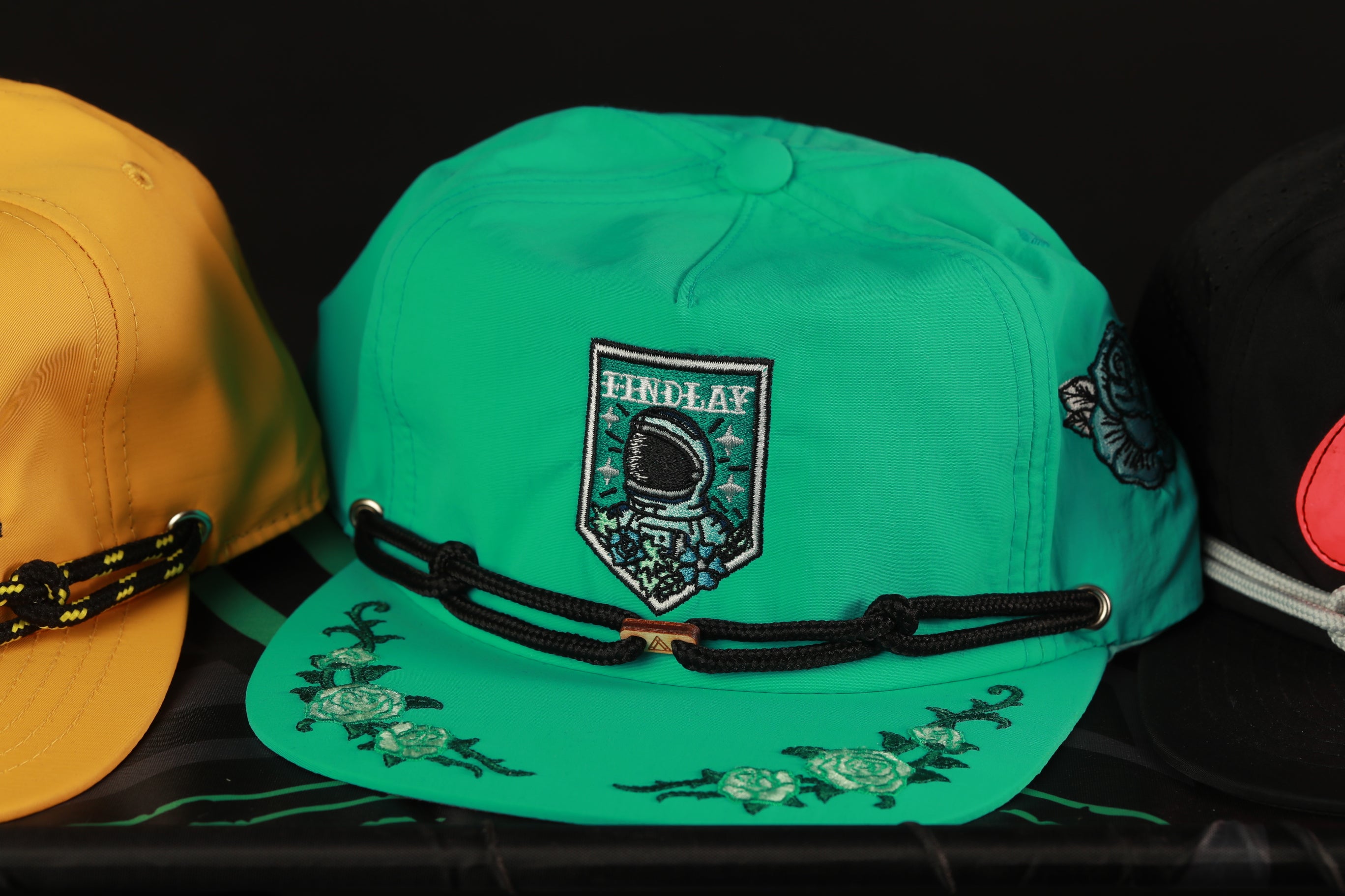 A close-up image of a green baseball cap with a floral design and a patch that says "HINDLAY" on it.