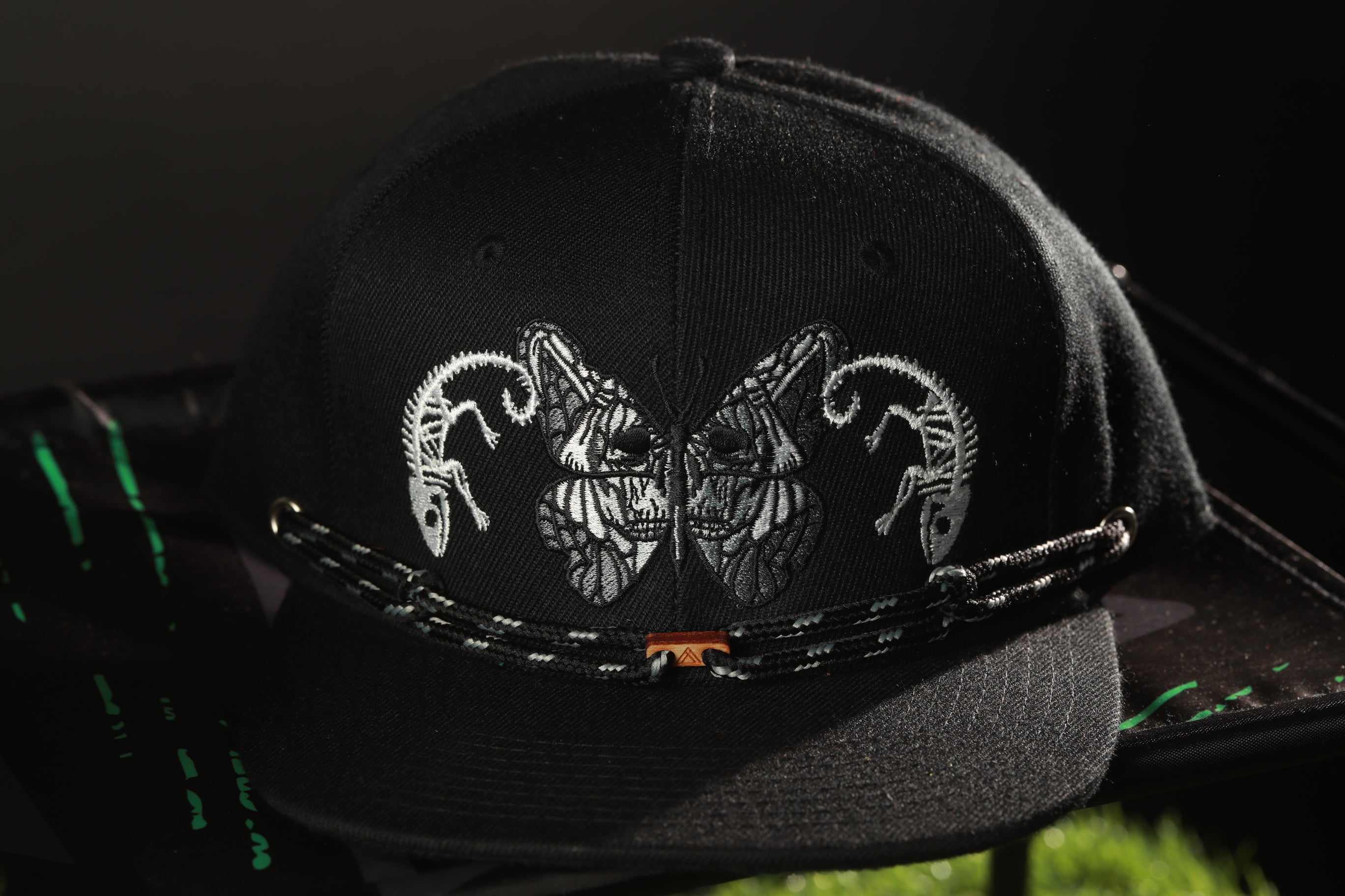 A black baseball cap with a unique design featuring two stylized animal faces, possibly a chameleon or a similar creature, on the front.
