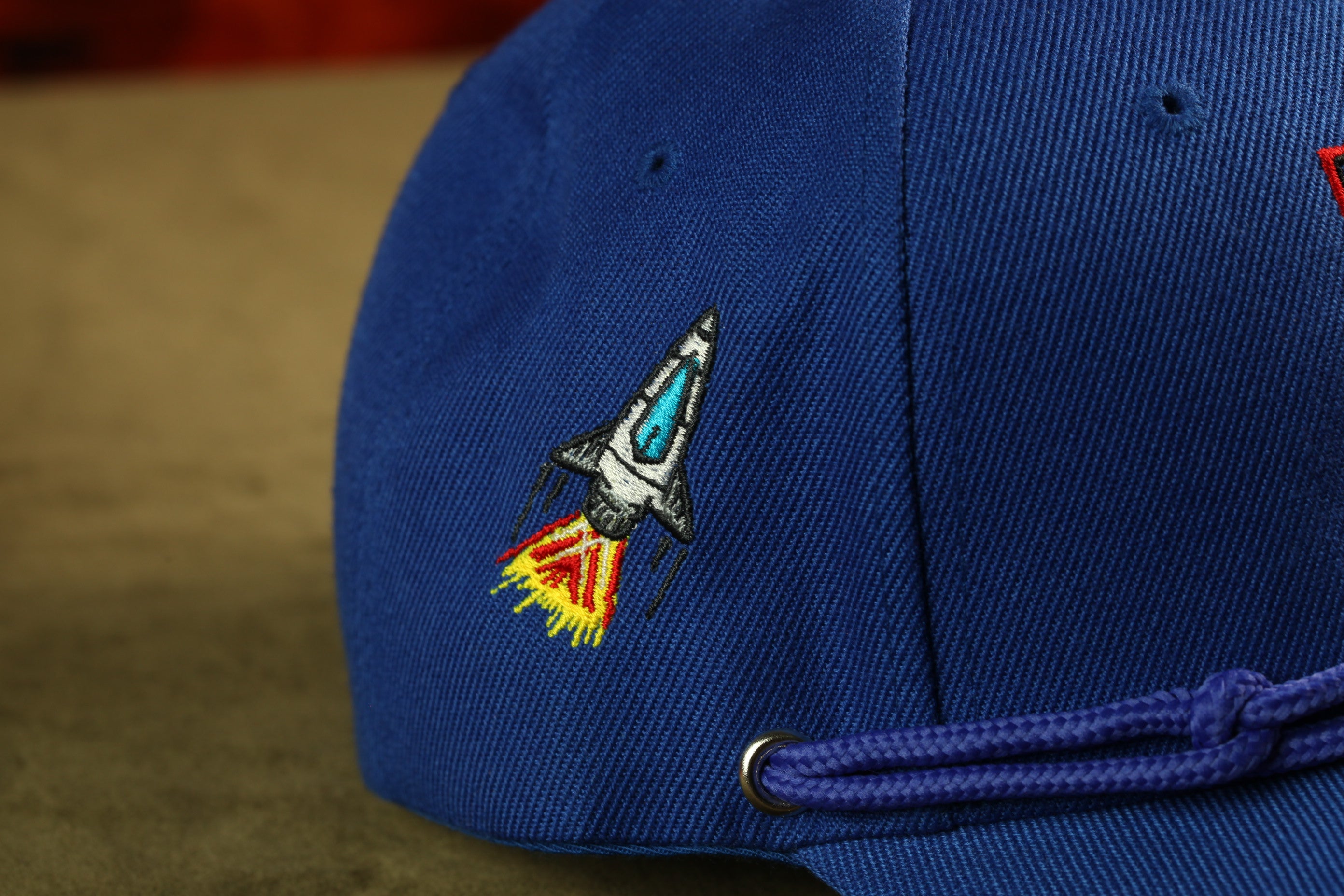 A close-up view of a blue baseball cap with a rocket ship embroidered on it.