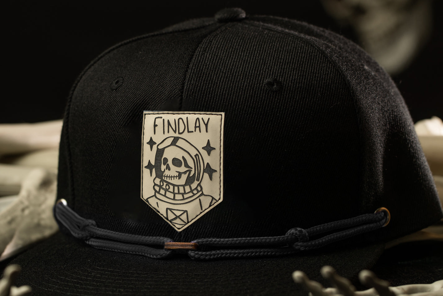 A black baseball cap with a white patch featuring a skull and stars, along with the text "FINDLAY" printed on it.