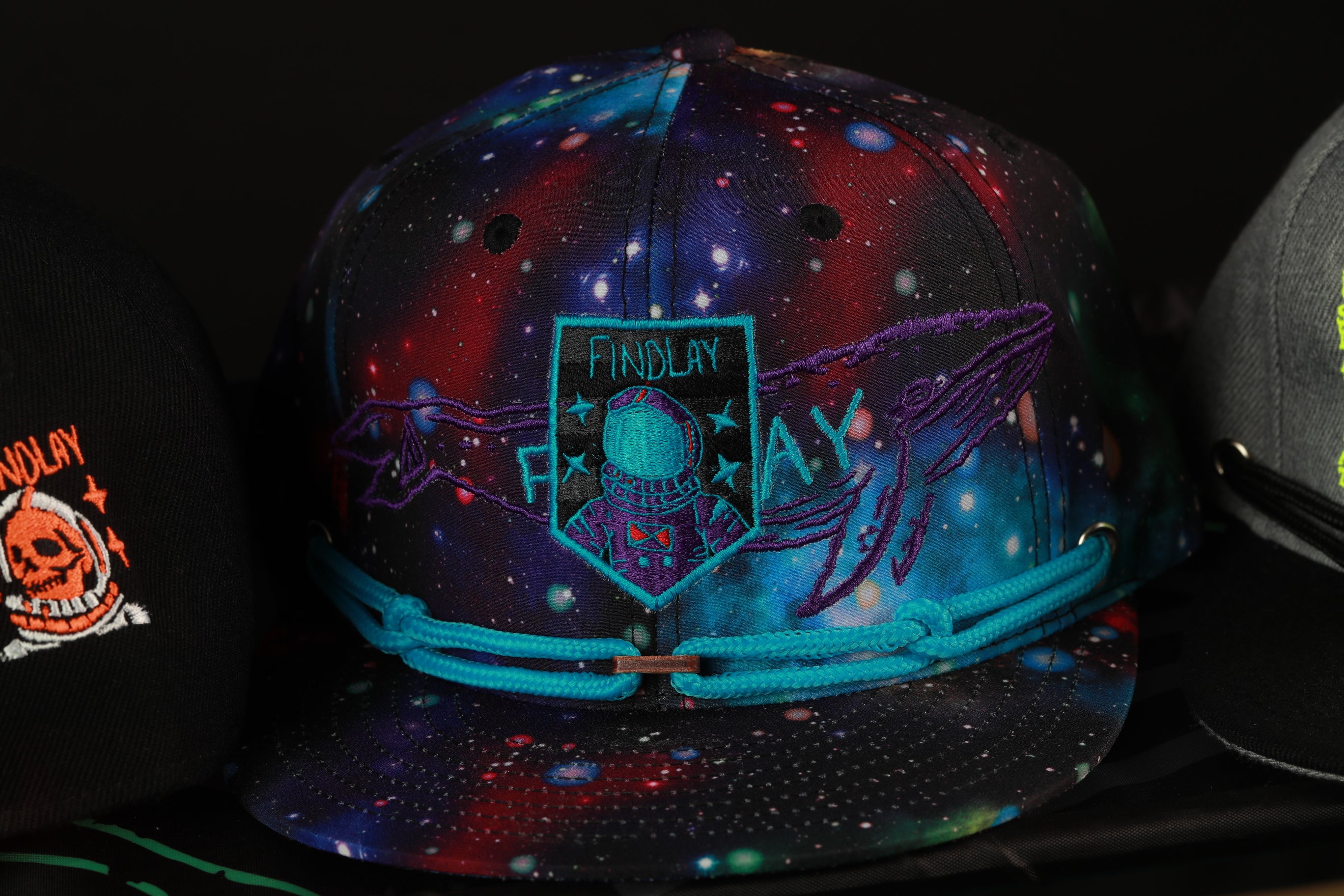 A colorful baseball cap with a space-themed design, featuring a patch with the text "FINDlay" and an image of a person in a spacesuit.