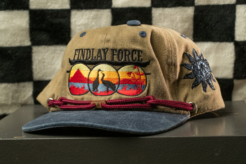 A tan baseball cap with a blue brim and a maroon string, featuring a colorful embroidered design and the text "Findlay Force" on the front.