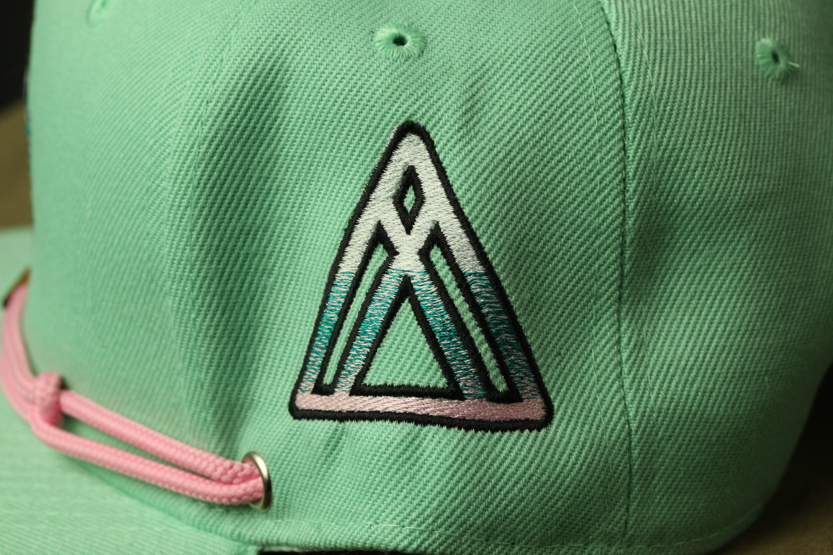 A close-up view of a green baseball cap with a pink string.