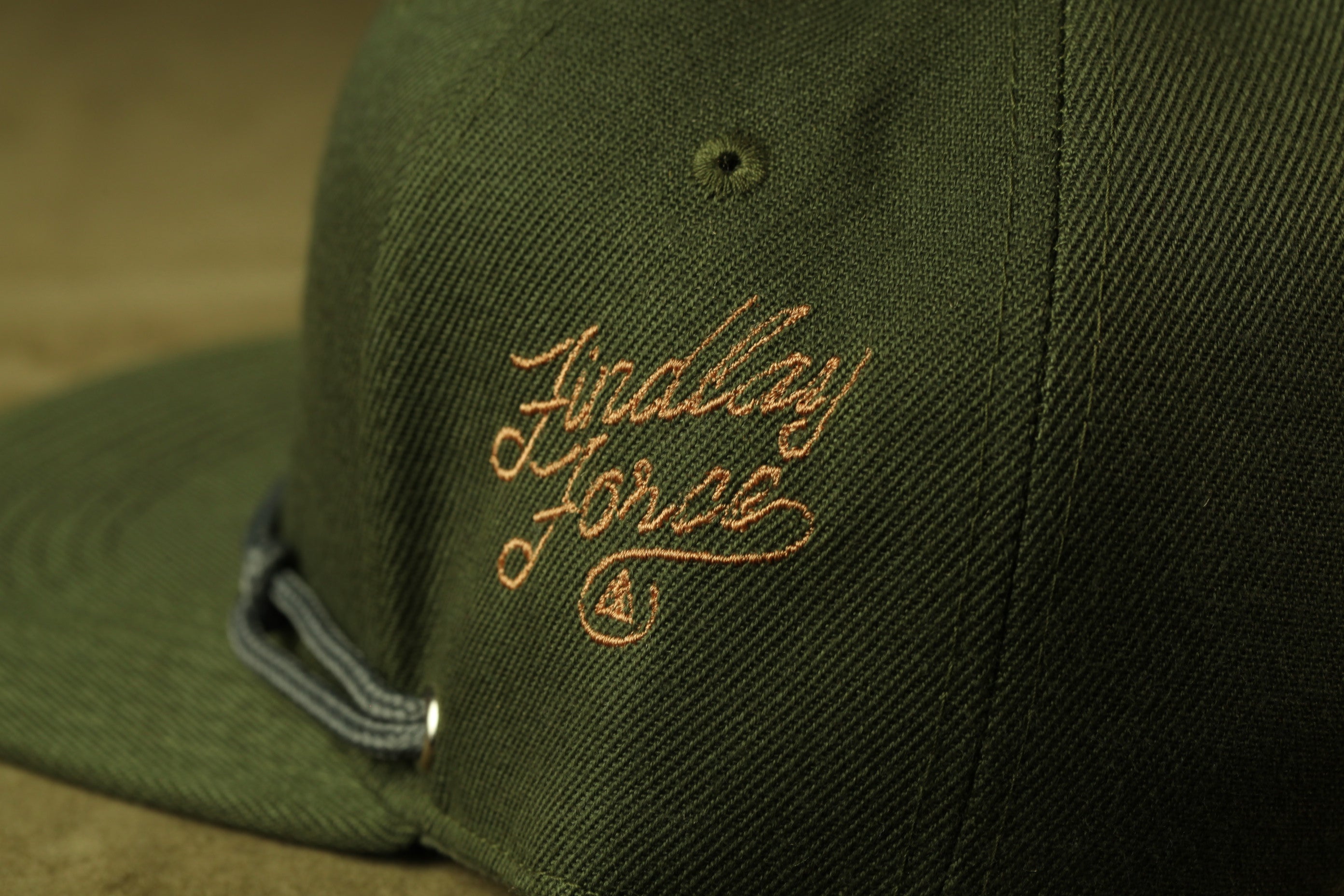 A close-up view of a green baseball cap with an embroidered logo on the front.