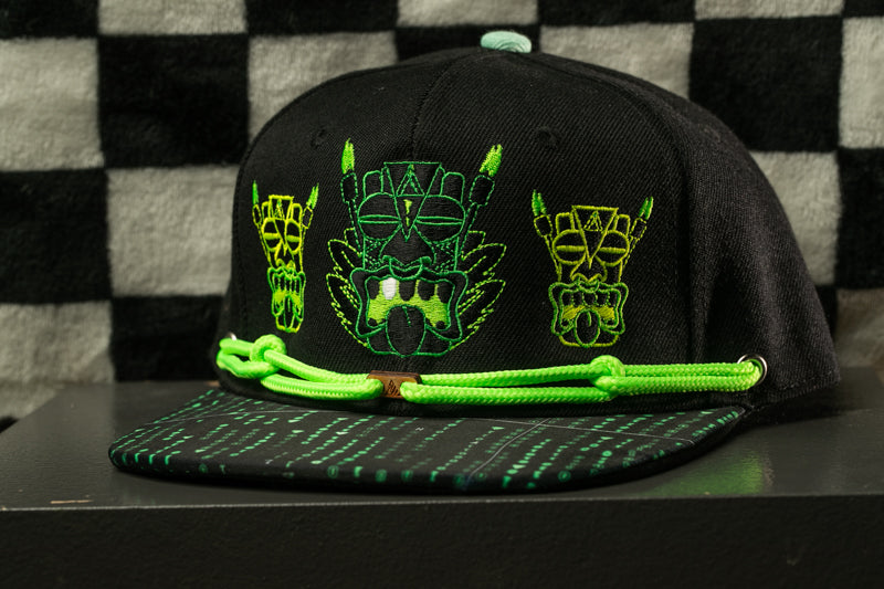 A black baseball cap with green and yellow designs on the front, including a mask-like figure and a skull-like figure.