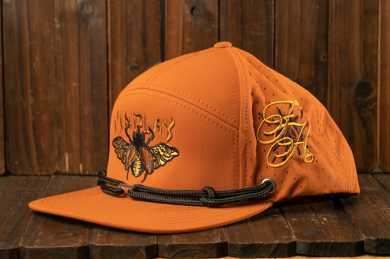 An orange baseball cap with a black strap and a detailed embroidered design on the front, placed on a wooden surface.