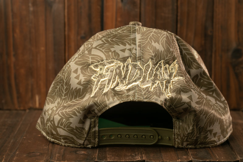 A camouflage-patterned baseball cap with the word "INDIA" embroidered on it, sitting on a wooden surface.
