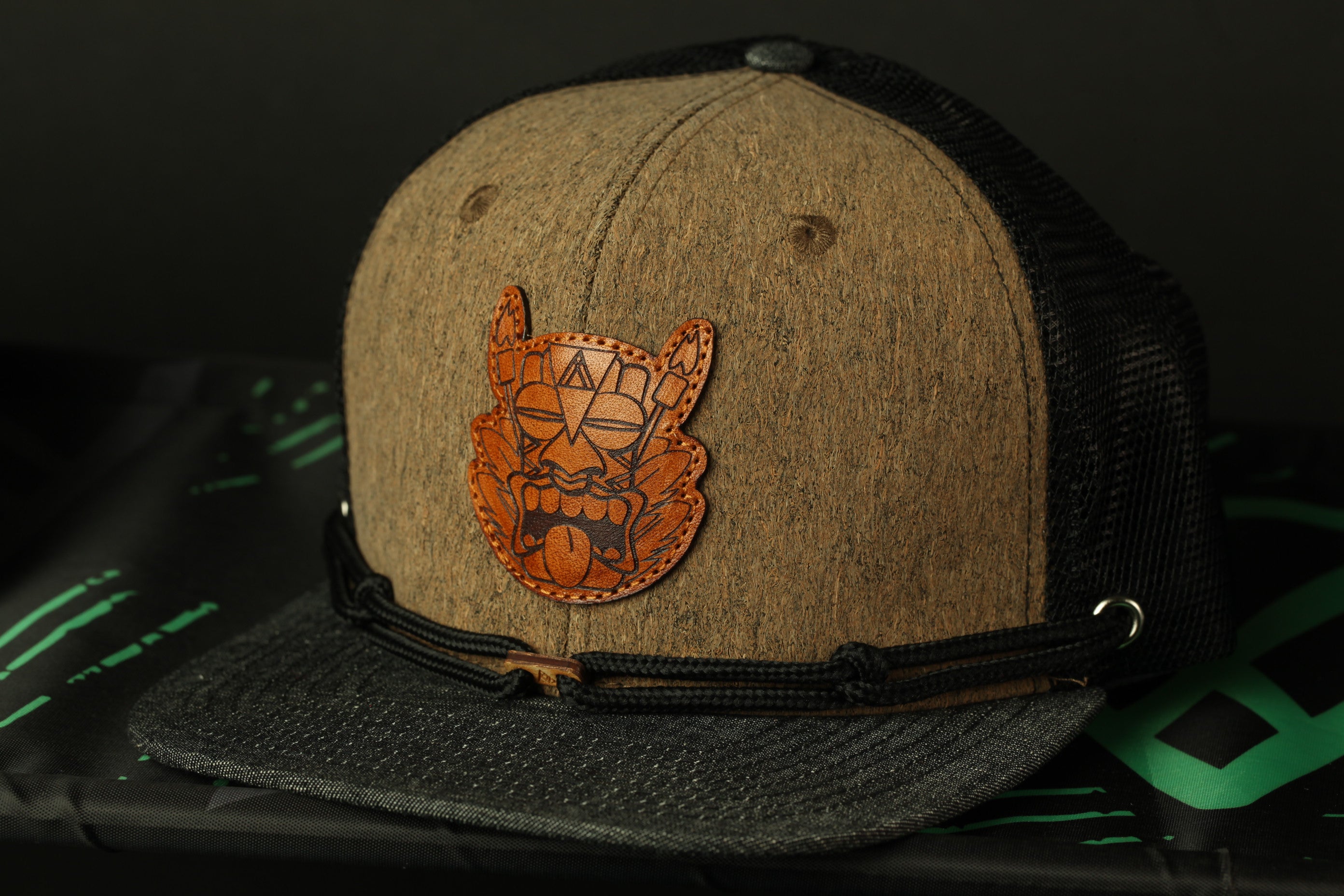 A brown baseball cap with a black mesh panel and a leather patch featuring an orange design on the front.