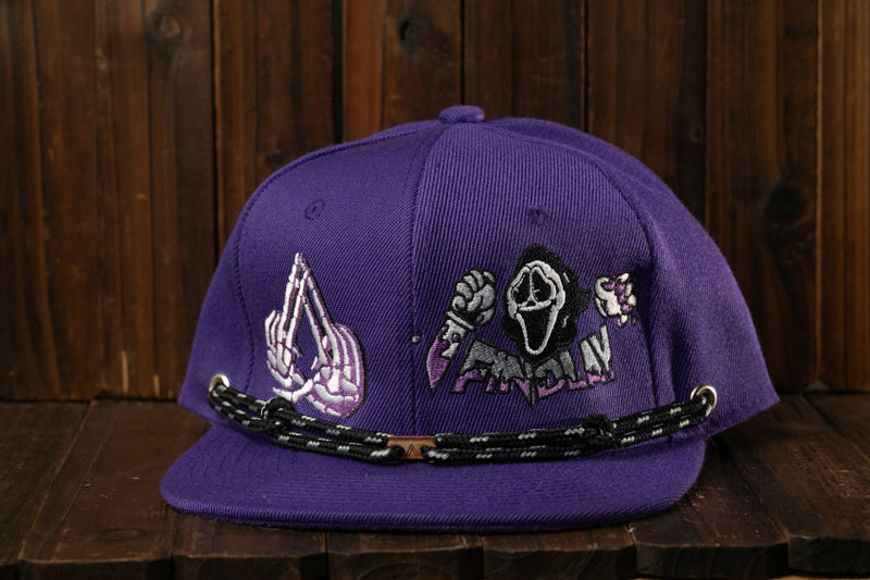 A purple baseball cap with a skull and crossbones design on it, sitting on a wooden surface.