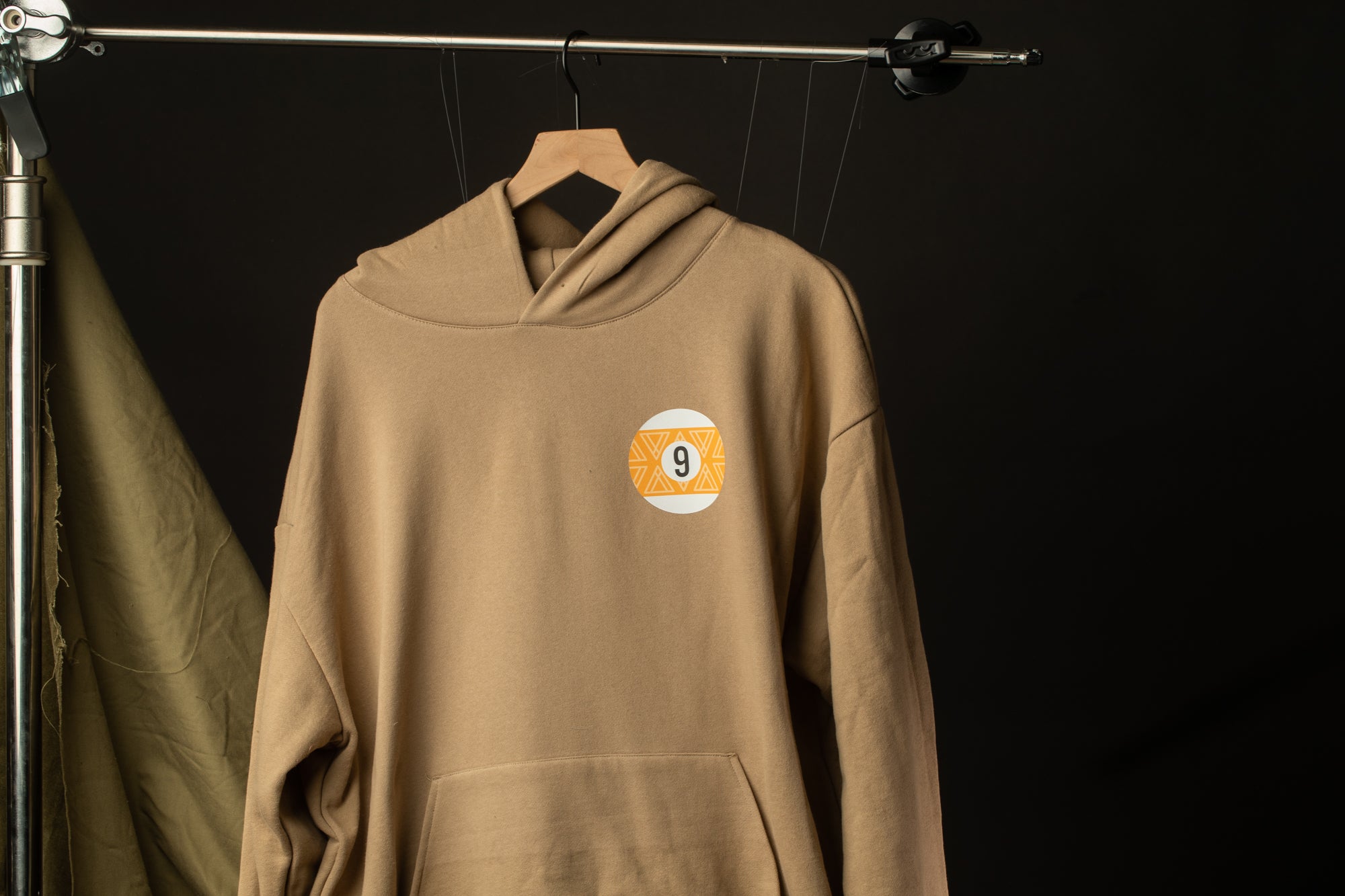 A beige hoodie with a number 9 on the front is hanging on a clothing rack against a dark background.