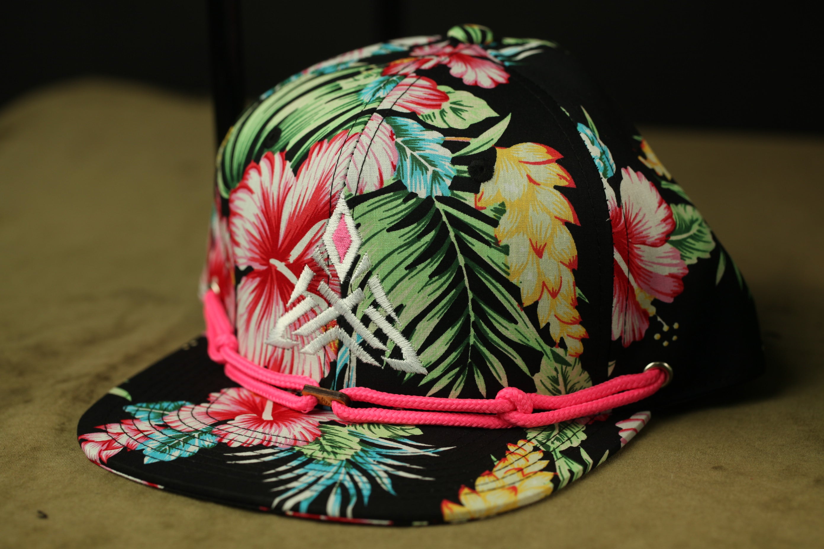 A colorful floral printed baseball cap with a pink braided strap.