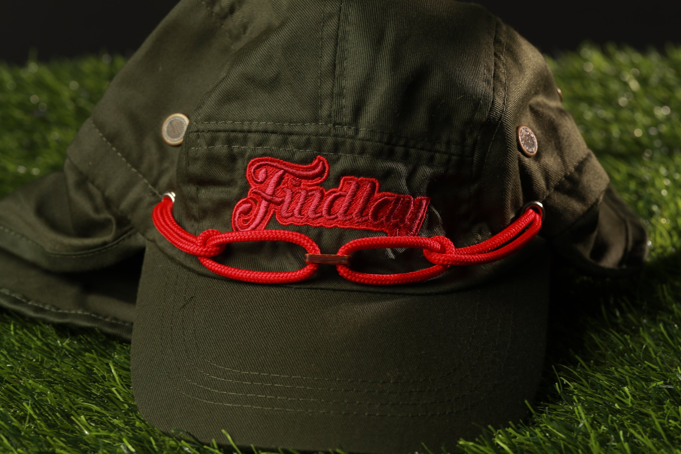 A green baseball cap with a red string and the word "Findlay" embroidered on it, placed on a grassy surface.