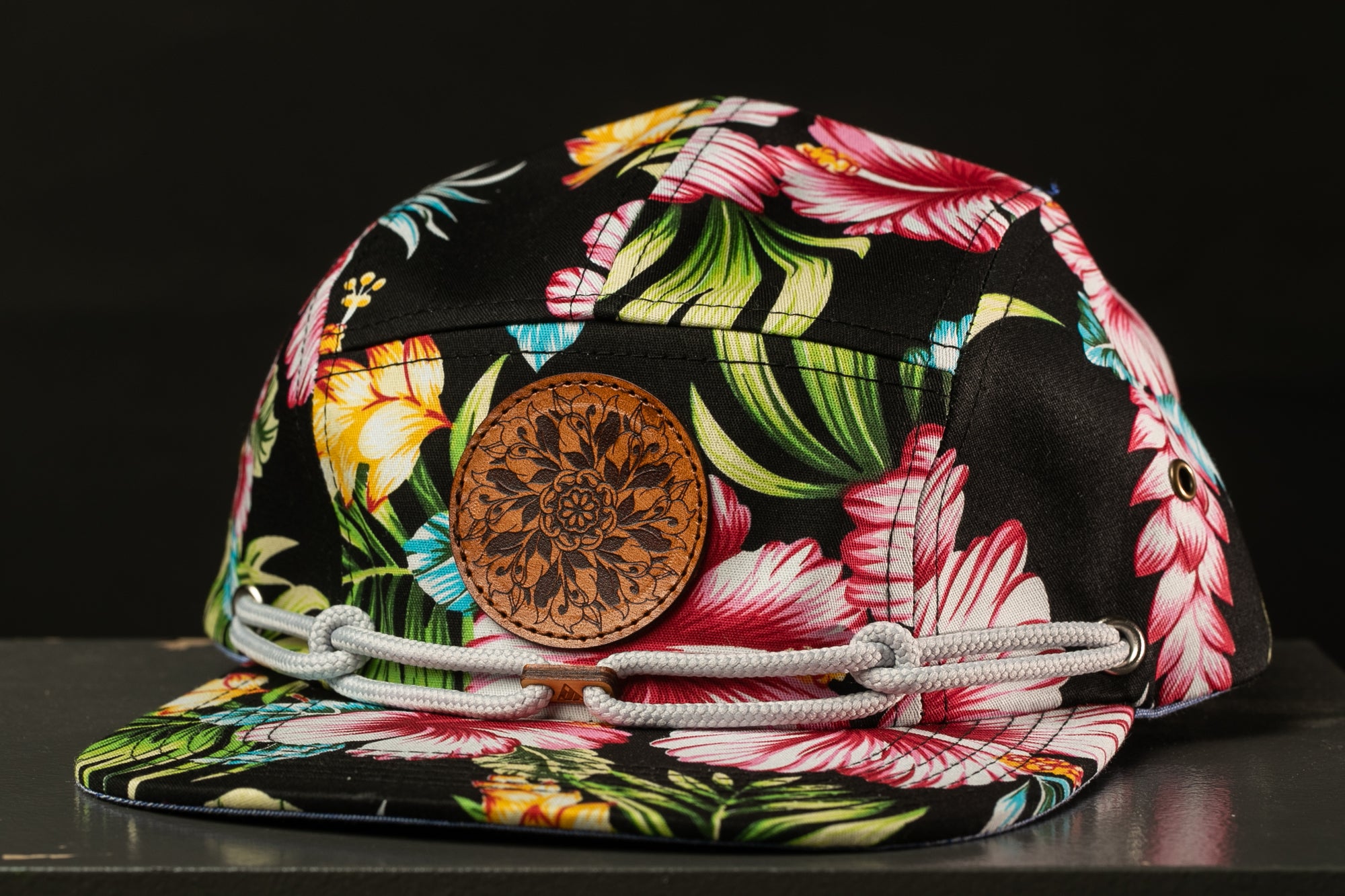 A colorful floral print cap with a brown leather patch and white straps.