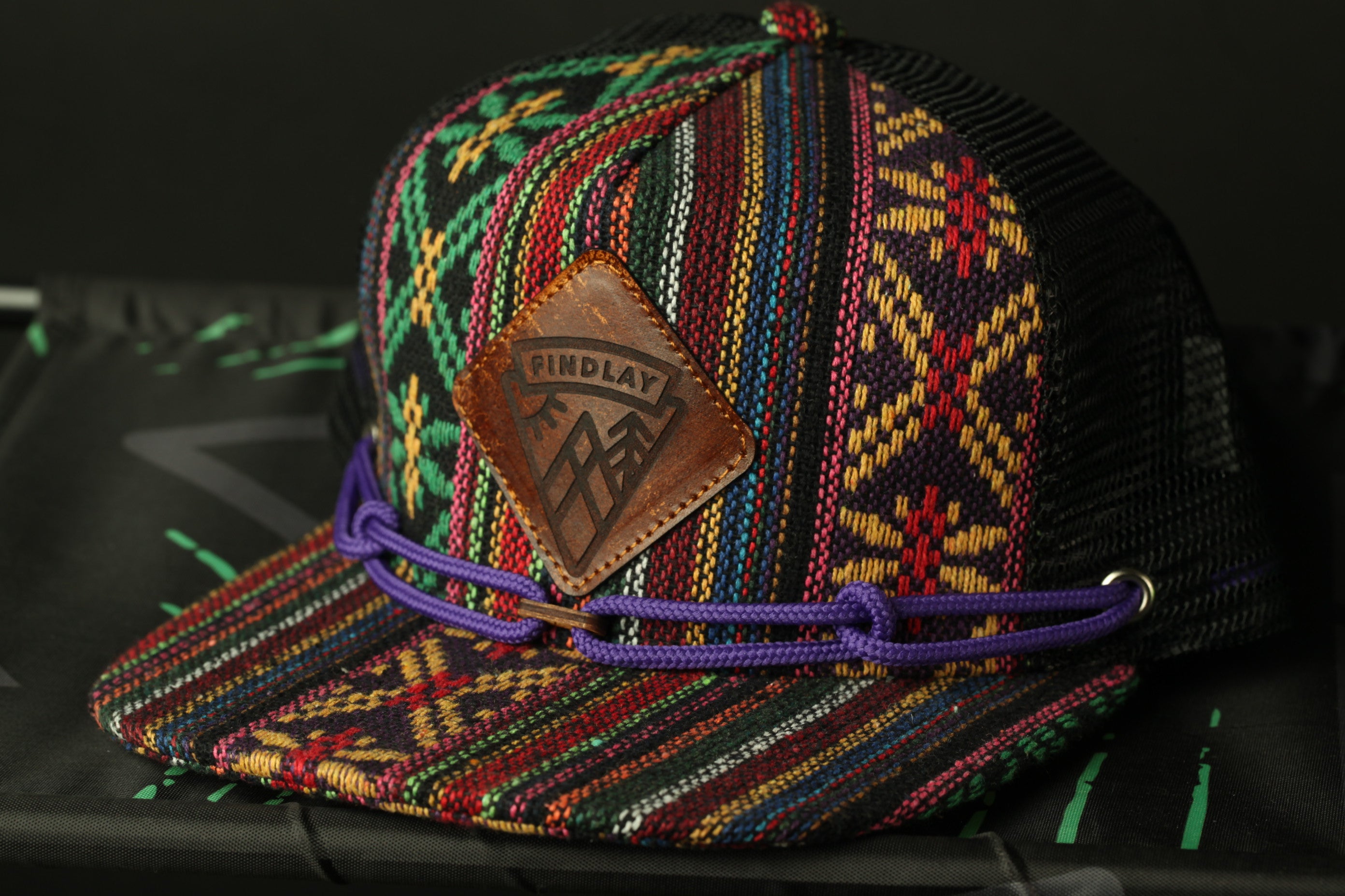 A colorful, patterned baseball cap with a leather patch and purple string.