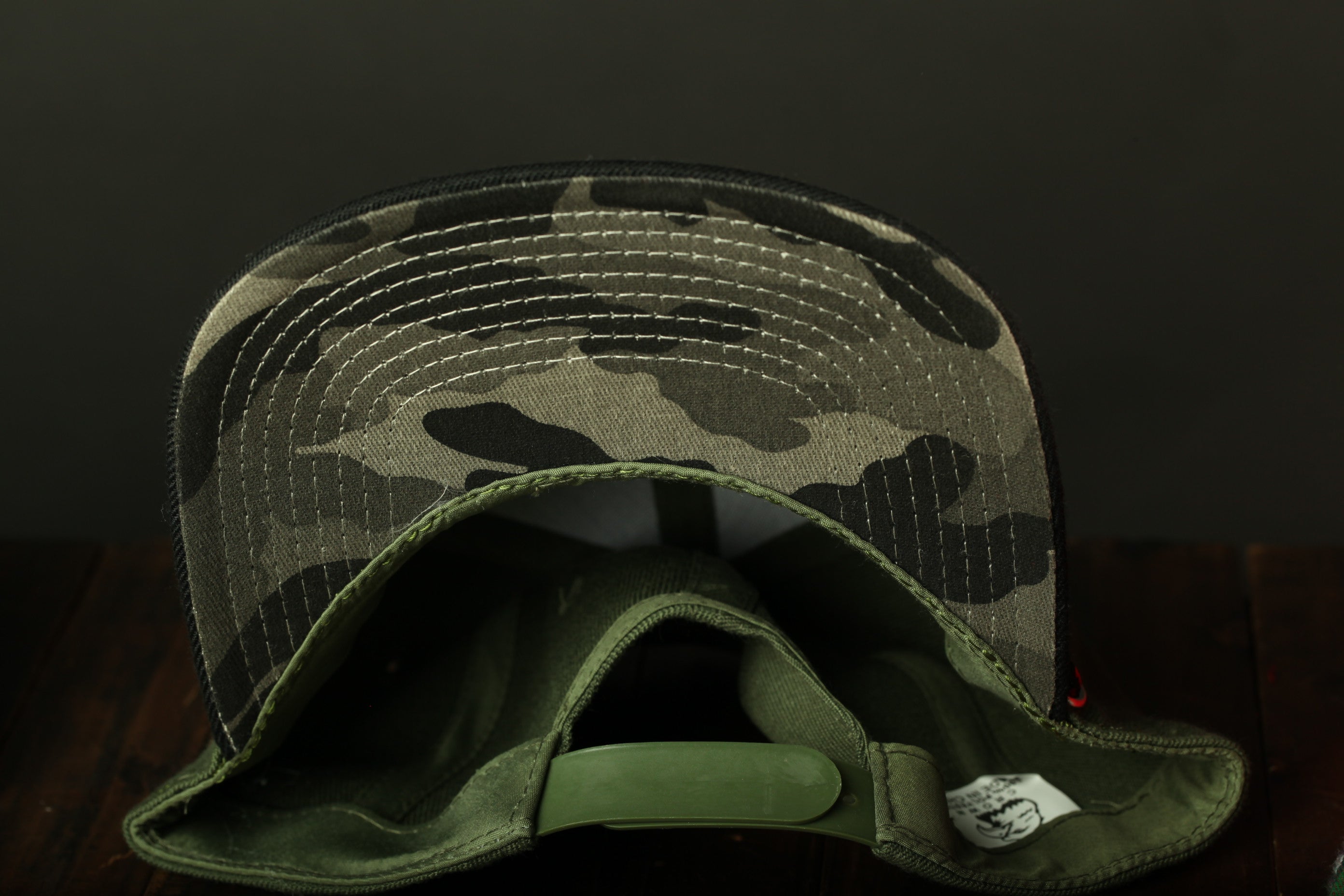 A camouflage-patterned baseball cap is shown in the image, with a green plastic strap visible inside the cap.