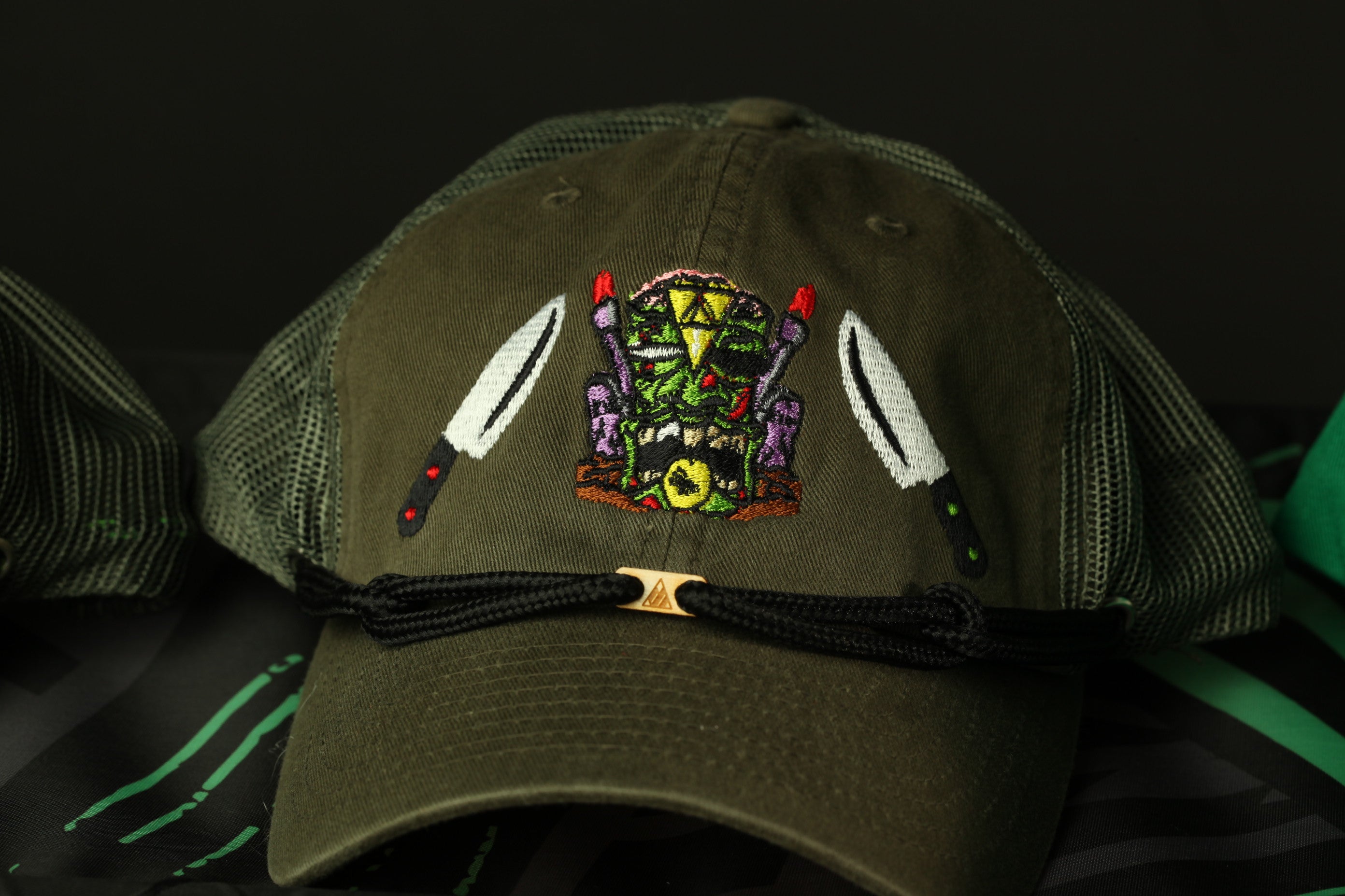 A close-up view of a dark green baseball cap with a colorful embroidered design on the front.