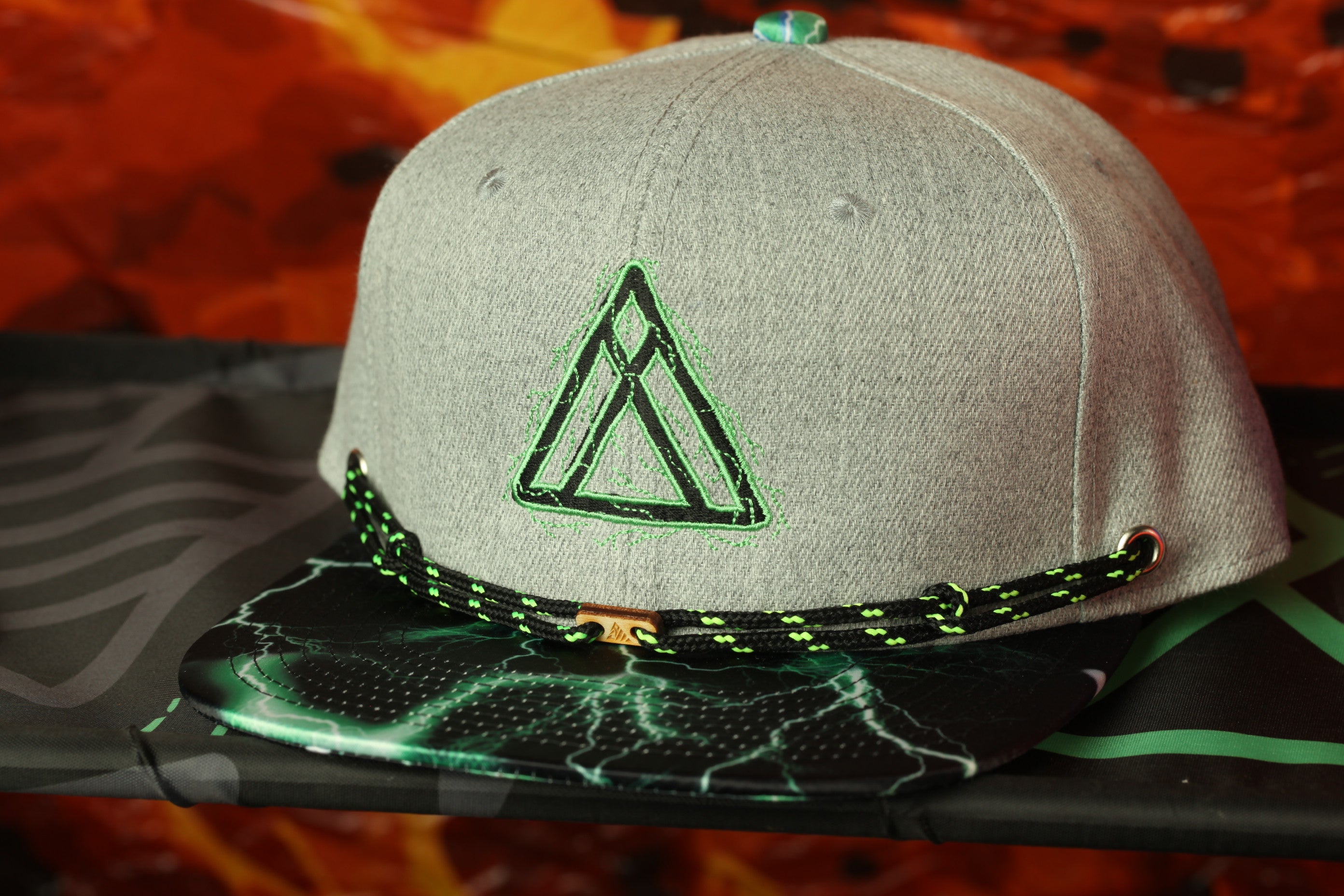 A gray baseball cap with a green triangle logo on the front, placed on a black surface against a red background.