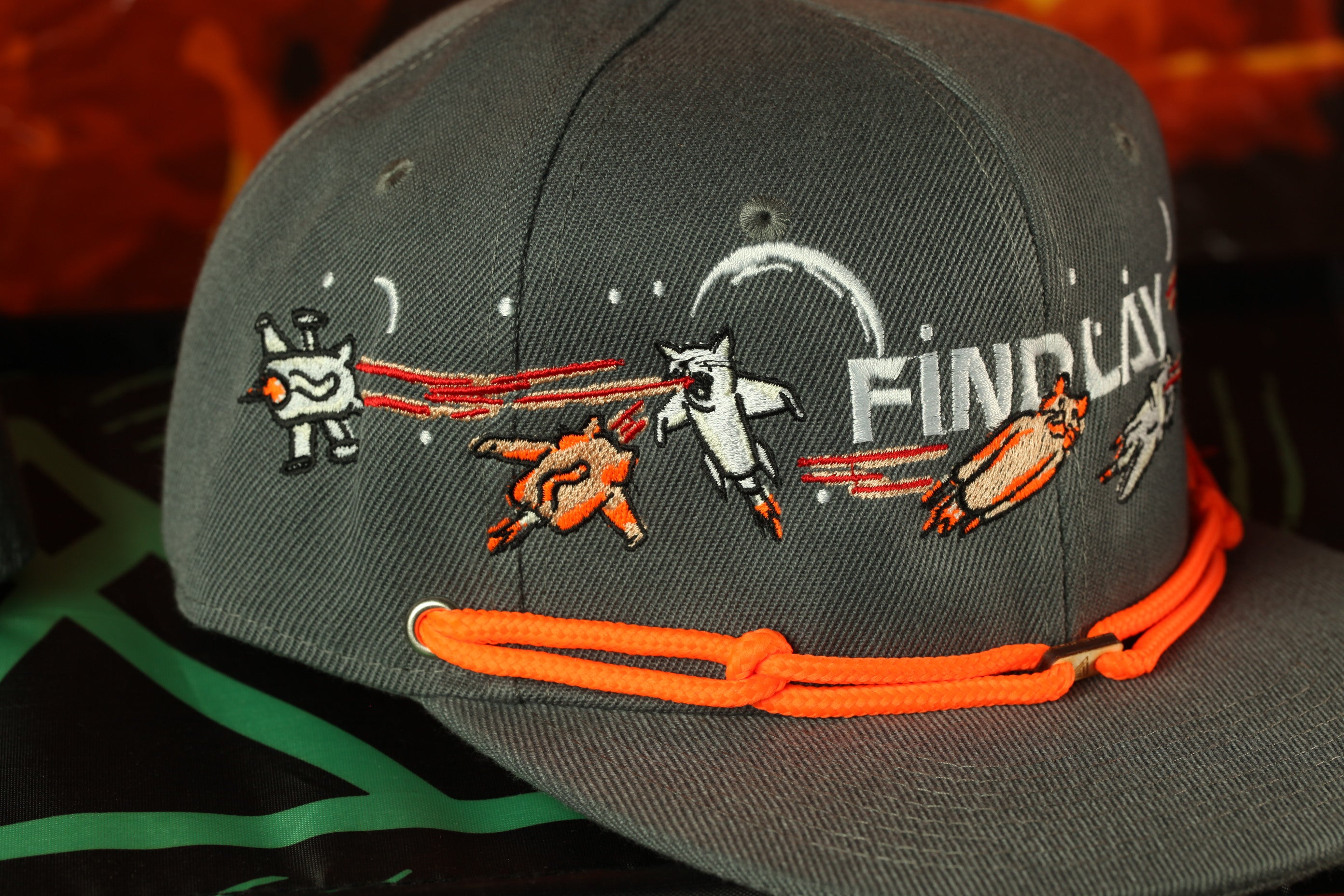 A gray baseball cap with a unique embroidered design featuring a cat, a rocket, and a bird, along with the text "FIND LAY".
