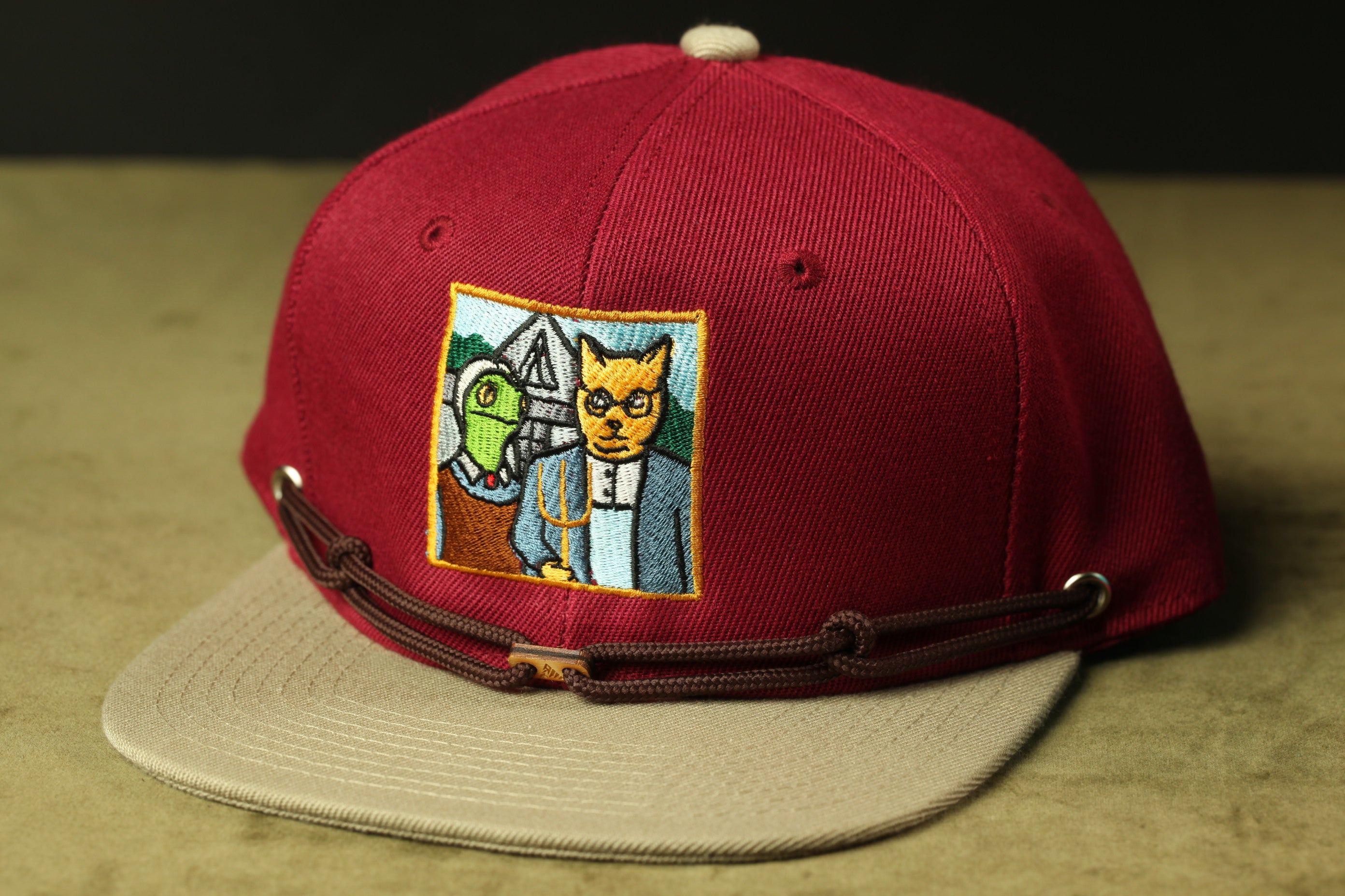 A red baseball cap with a cartoon cat and a green frog embroidered on it.
