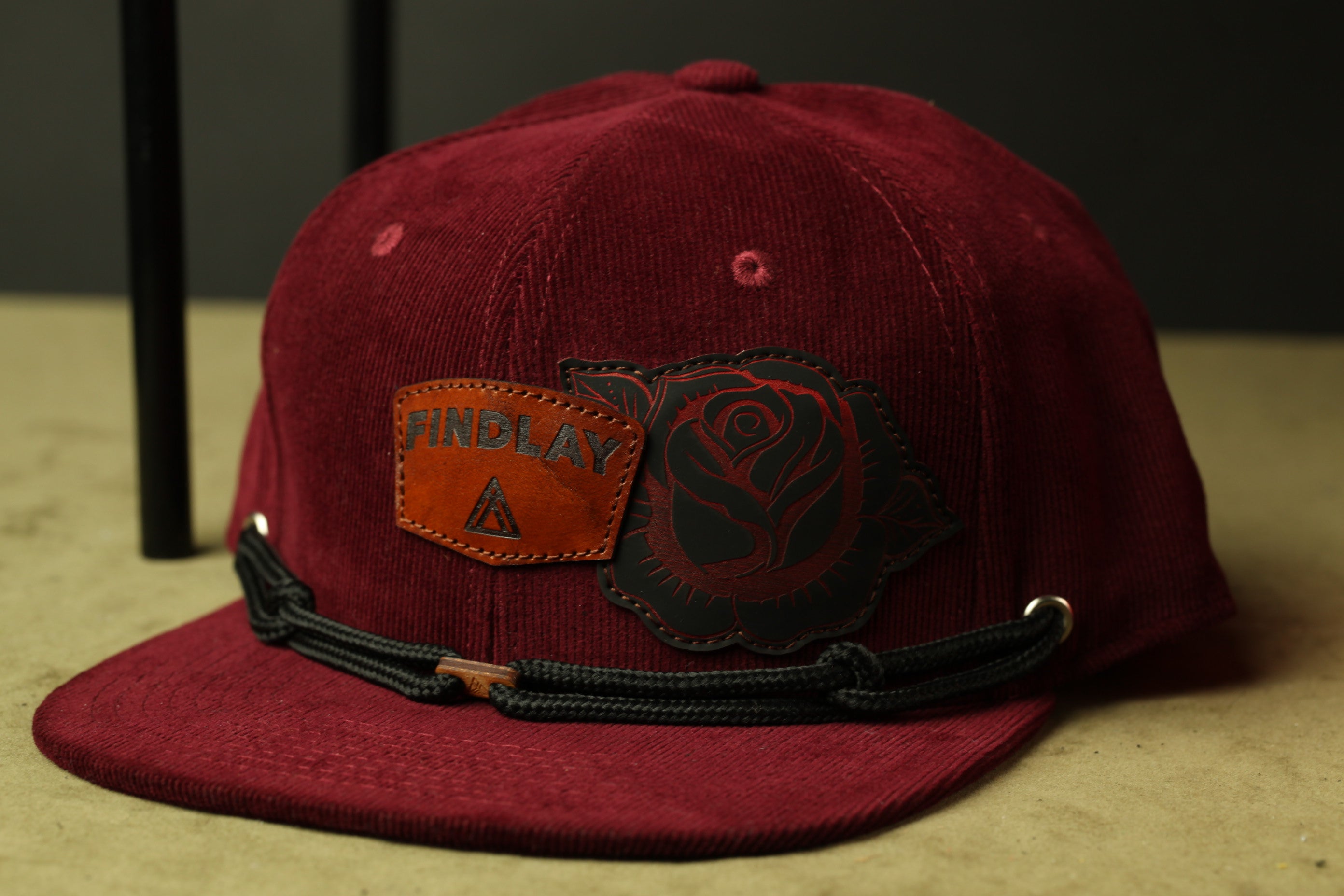 A burgundy baseball cap with a rose design and a leather patch on the front.