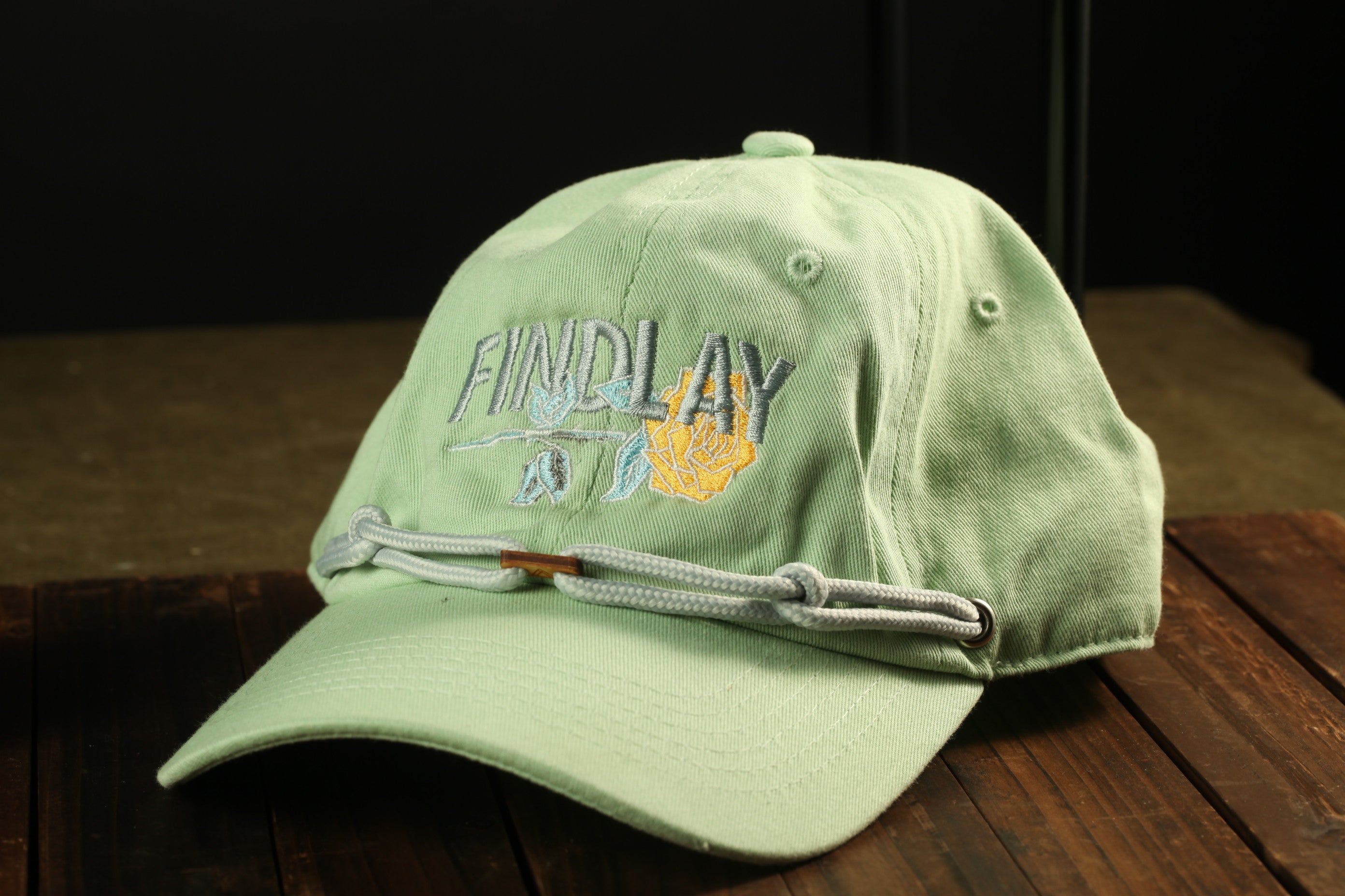 A green baseball cap with the text "FIND LAY" printed on it, sitting on a wooden surface.