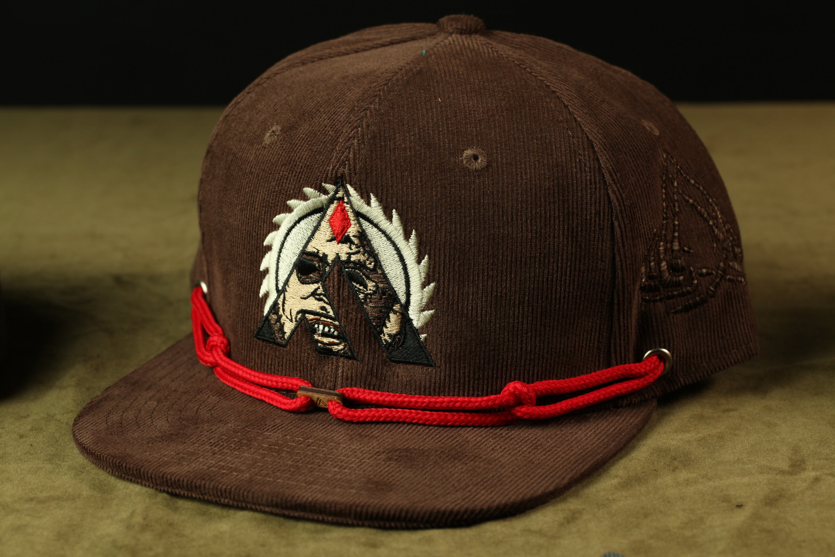 A brown baseball cap with a red string and an embroidered logo on the front.