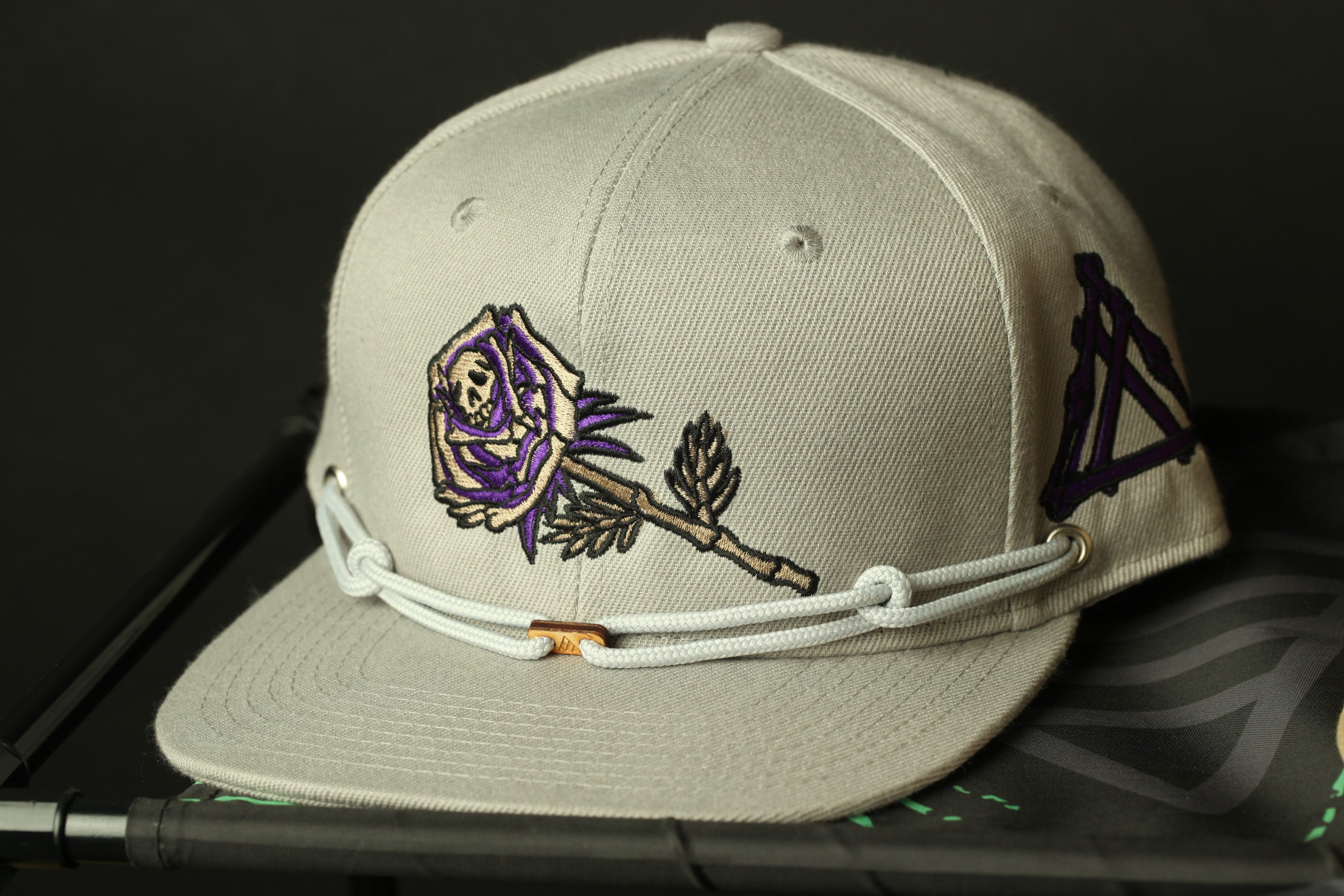 A beige baseball cap with a skull and rose embroidered on it, resting on a black surface.