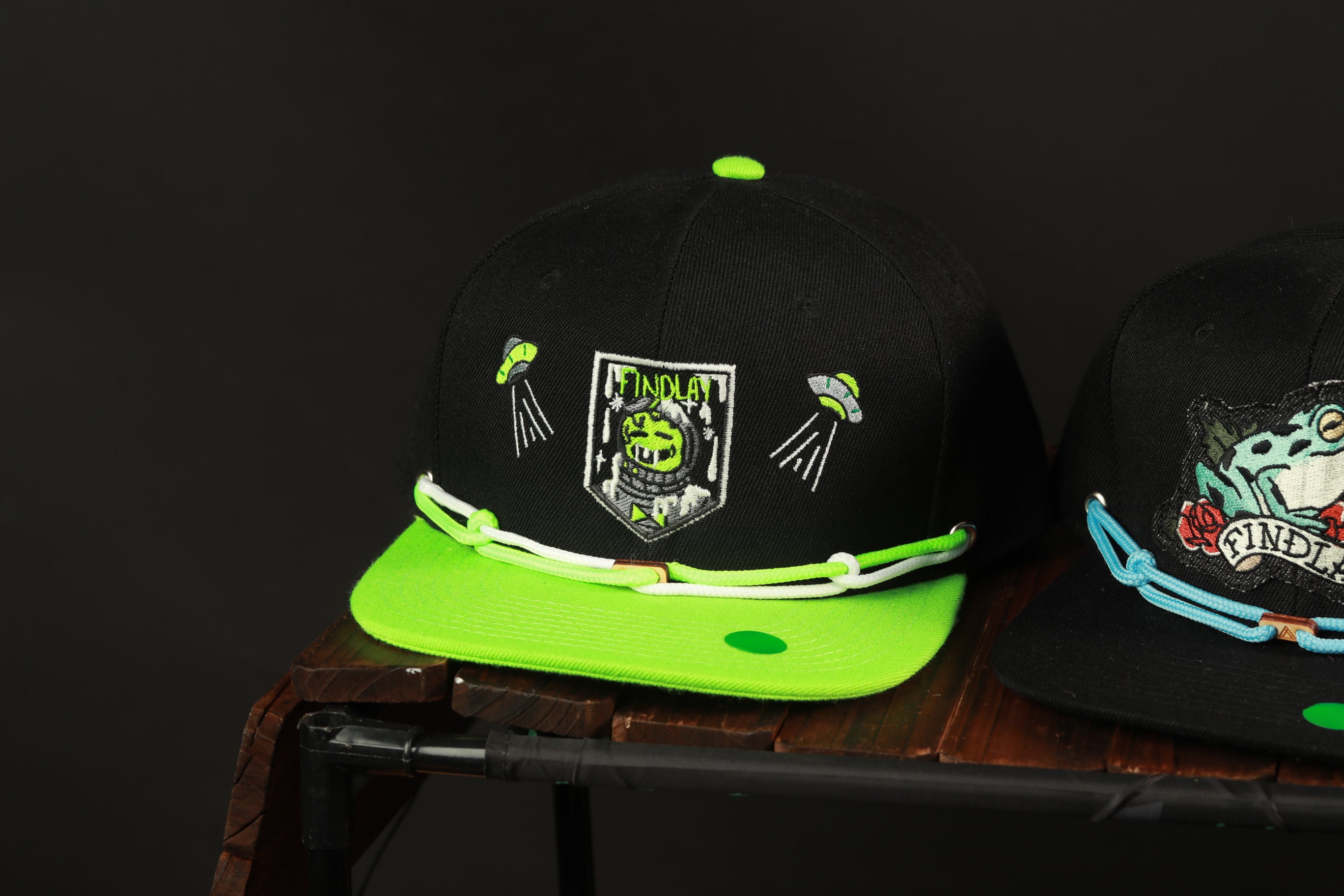 two baseball caps, one with a green brim and the other with a black brim, both displaying various designs and logos.