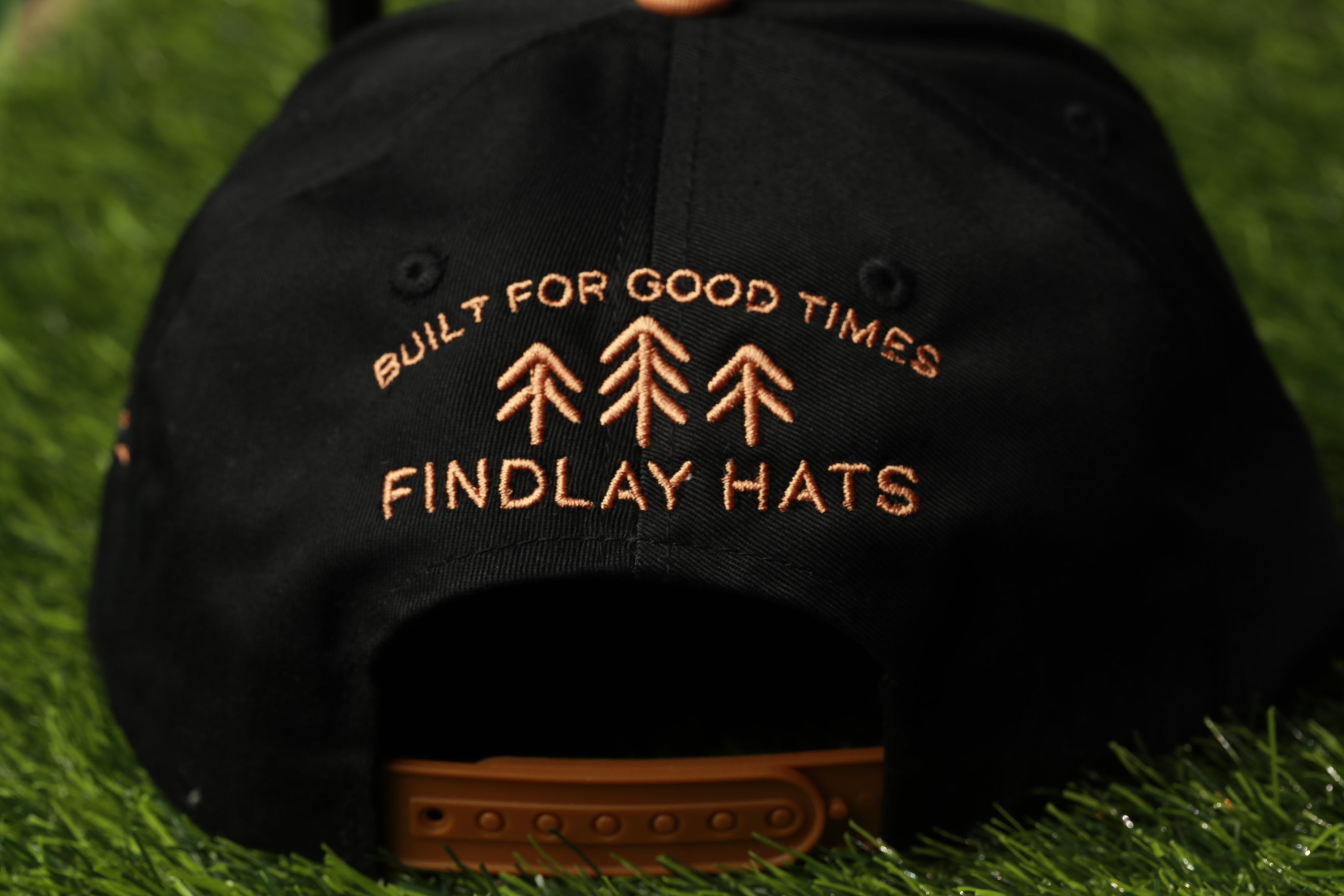 a black baseball cap with orange text and graphics on it, placed on a grassy surface.