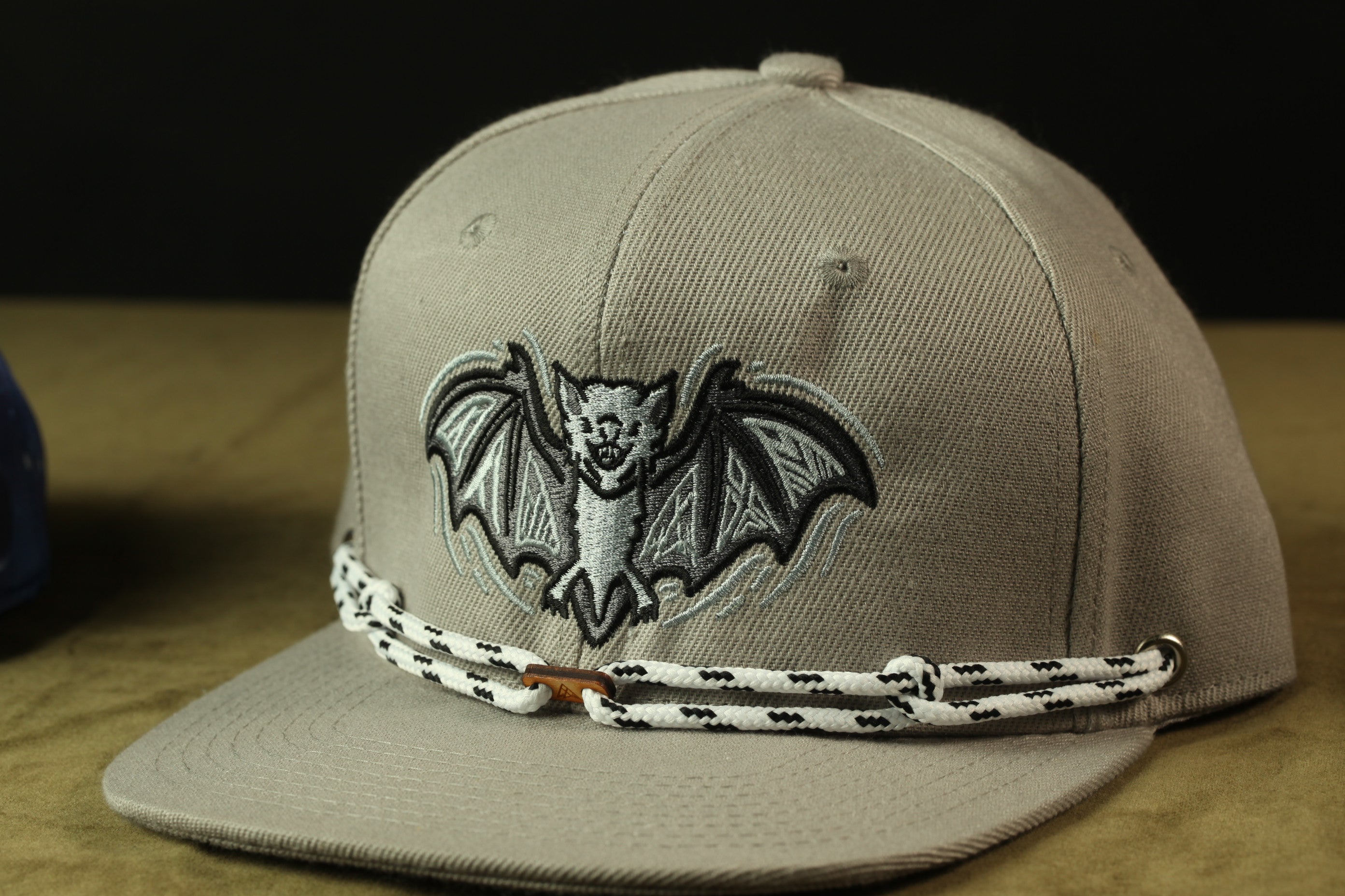 A gray baseball cap with a bat embroidered on it, sitting on a brown surface.