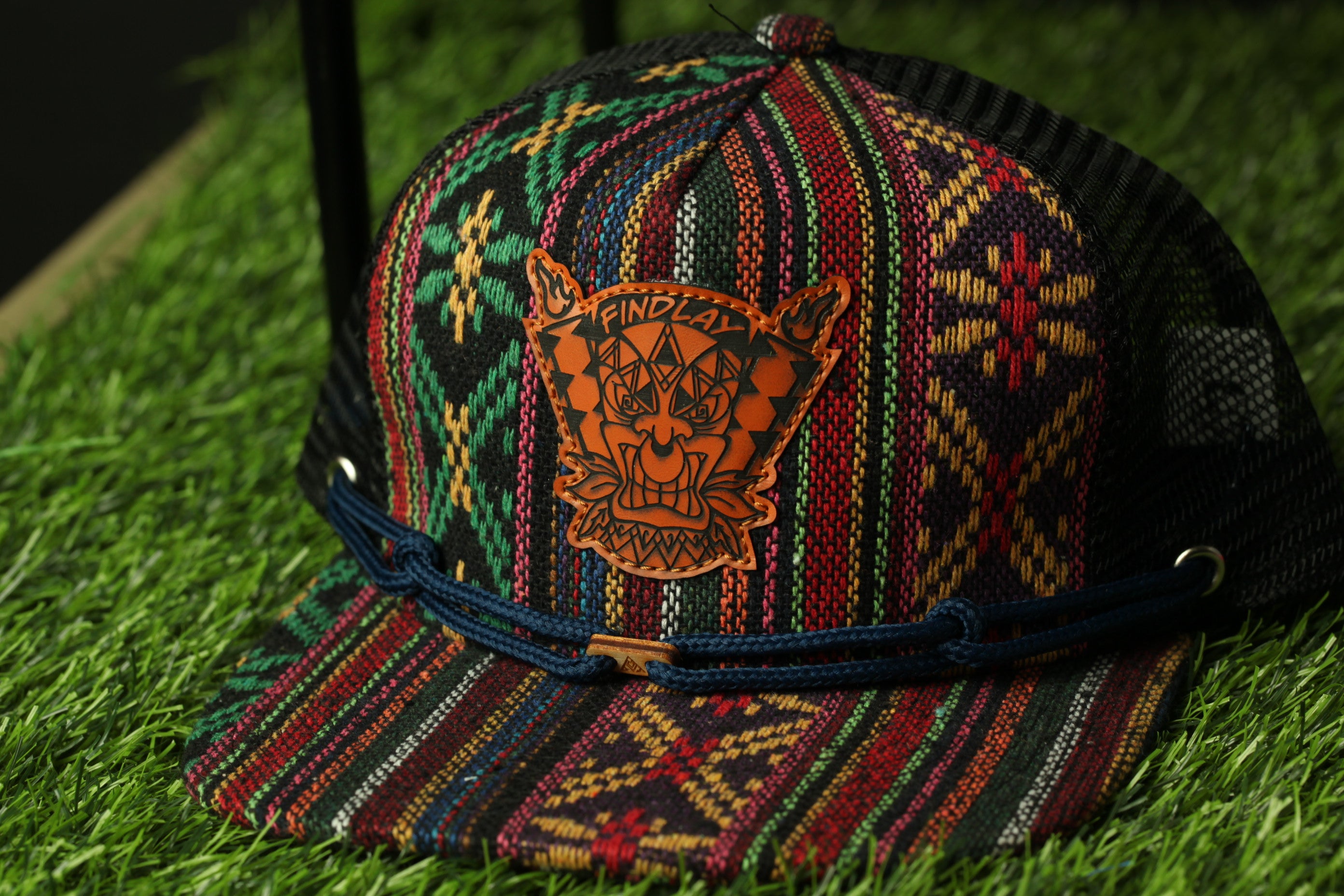 A colorful, patterned baseball cap with a distinctive orange and black design on the front, resting on a grassy surface.
